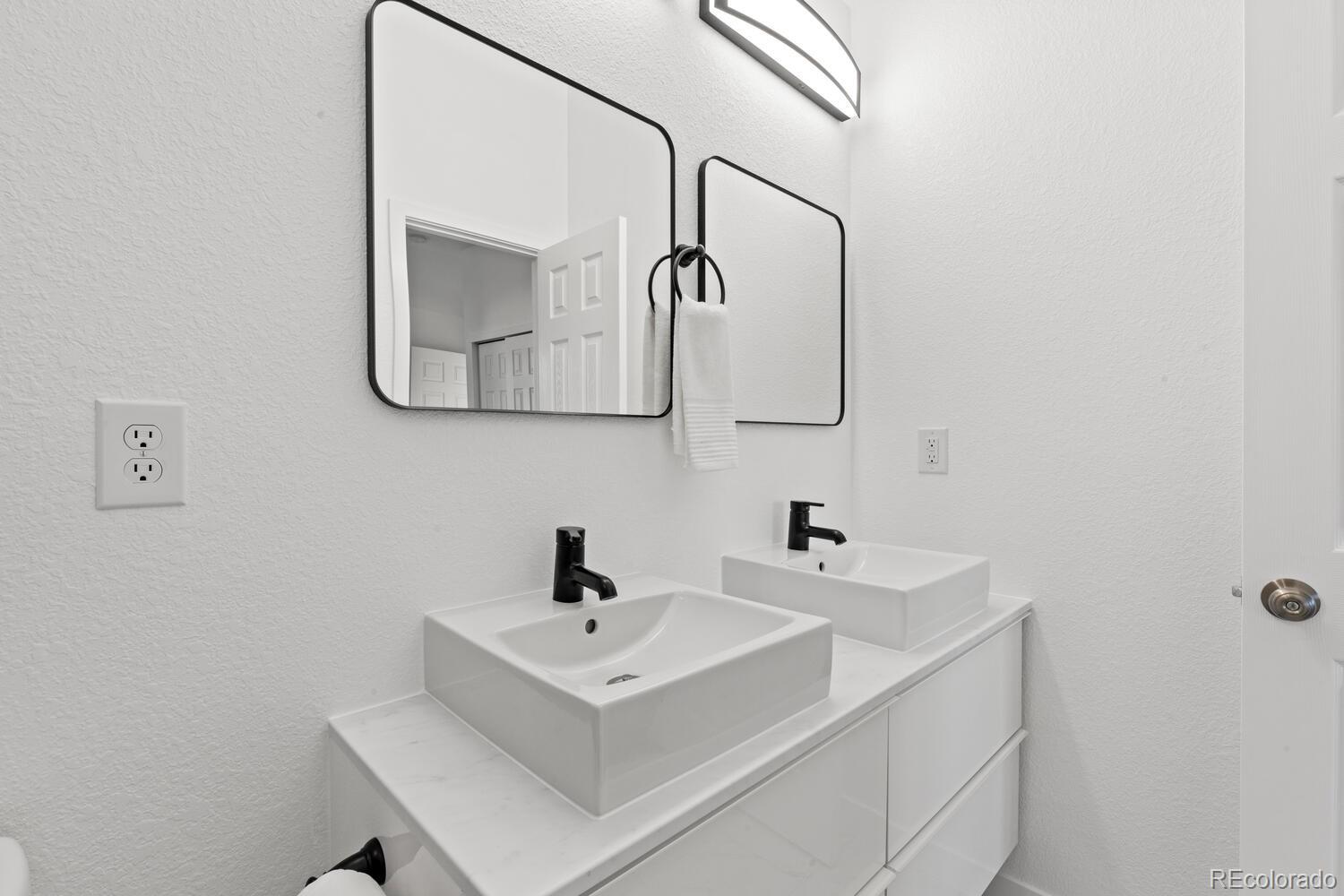 Bathroom vanity with two vessel sinks, black faucets, and large framed mirrors.