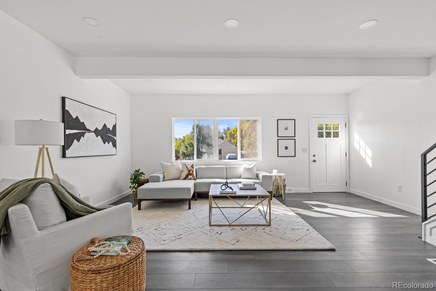 Staged living room with gray sectional, white rug, and sunlight streaming through a large window.