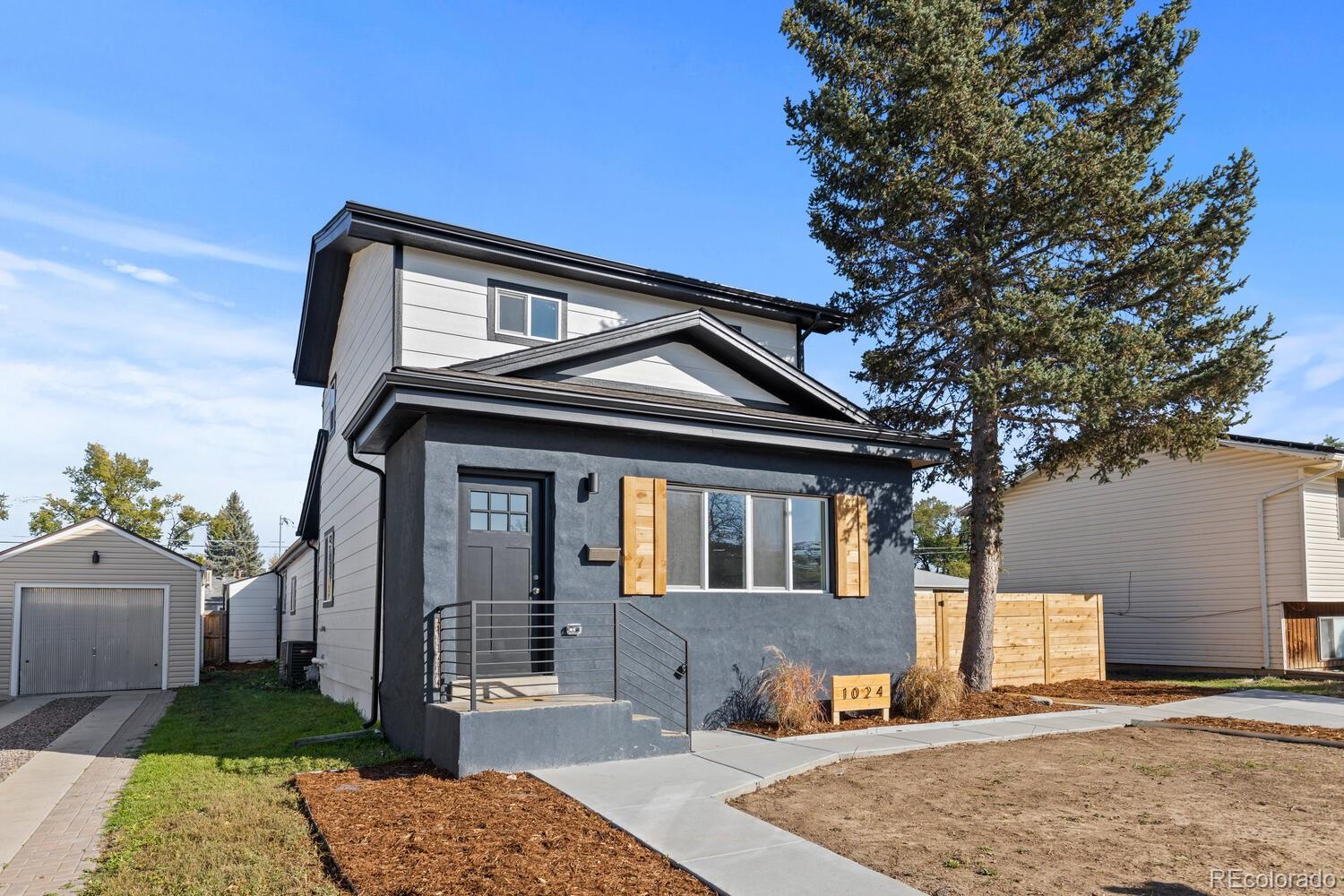 Modern two-story house with a dark gray facade, wood shutters, and a large evergreen tree.