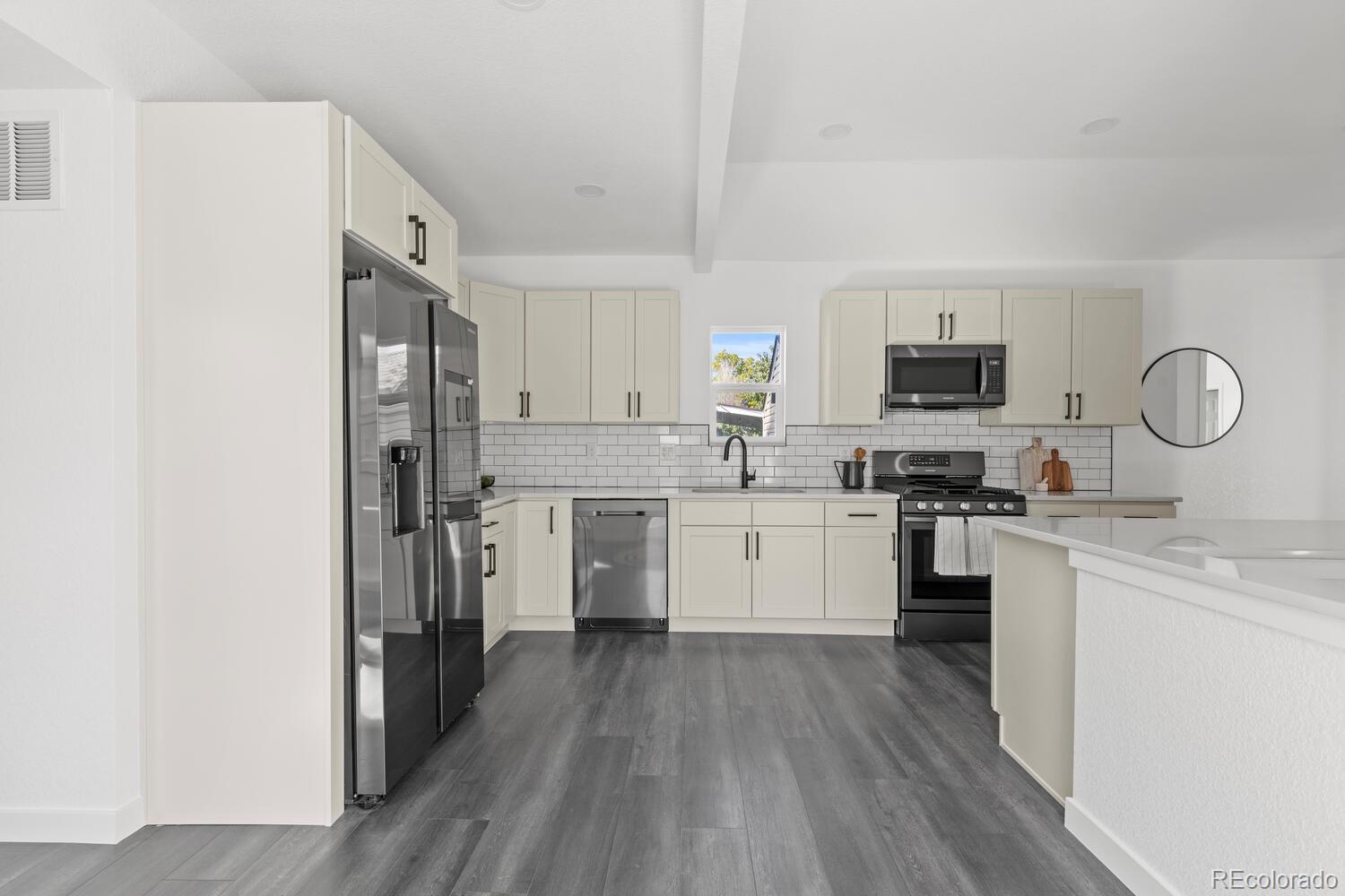 Kitchen with cream cabinets, stainless steel appliances, white subway tile backsplash, and dark gray plank flooring.