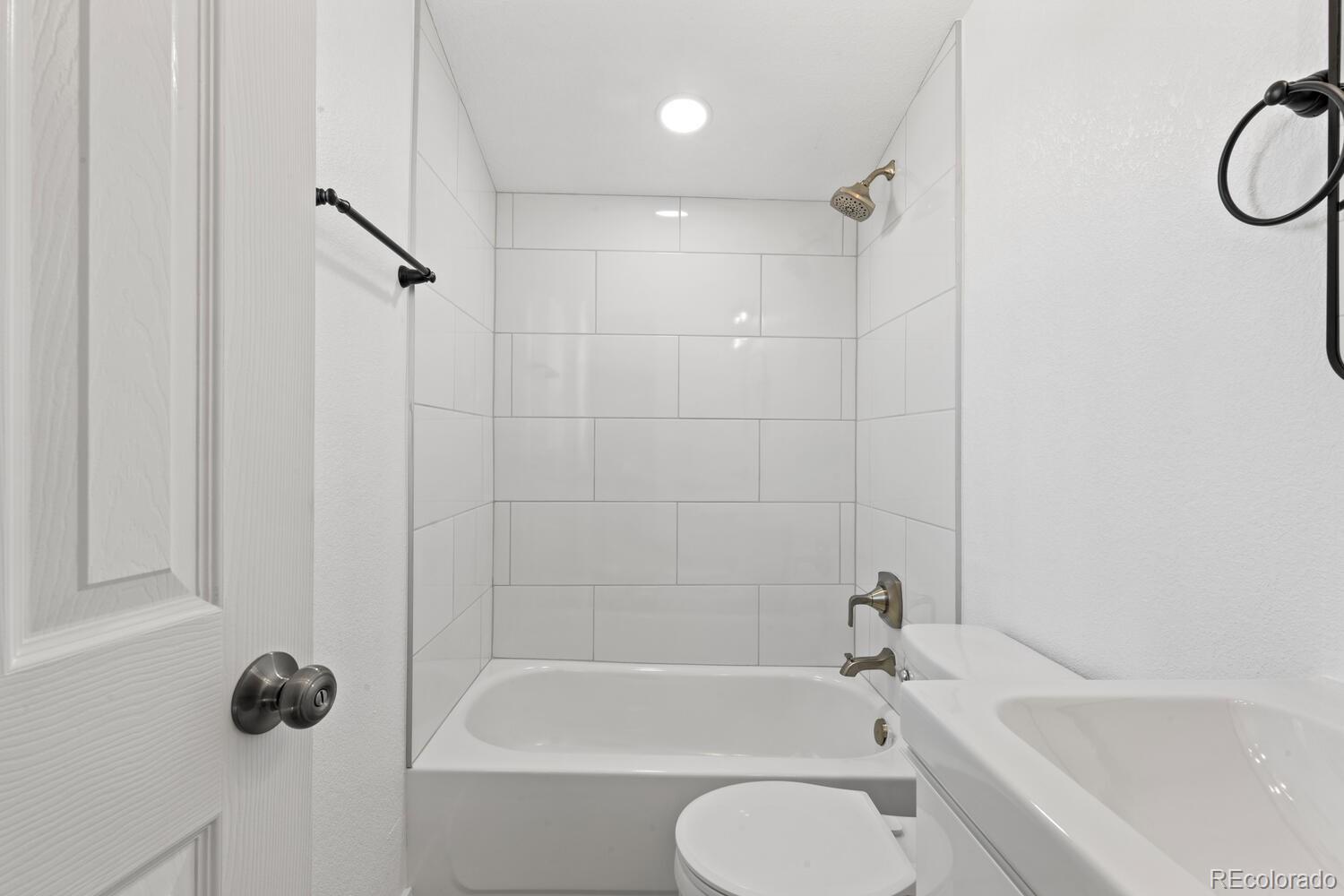Bathroom with a white tiled tub and shower, brass fixtures, and a white sink and toilet.