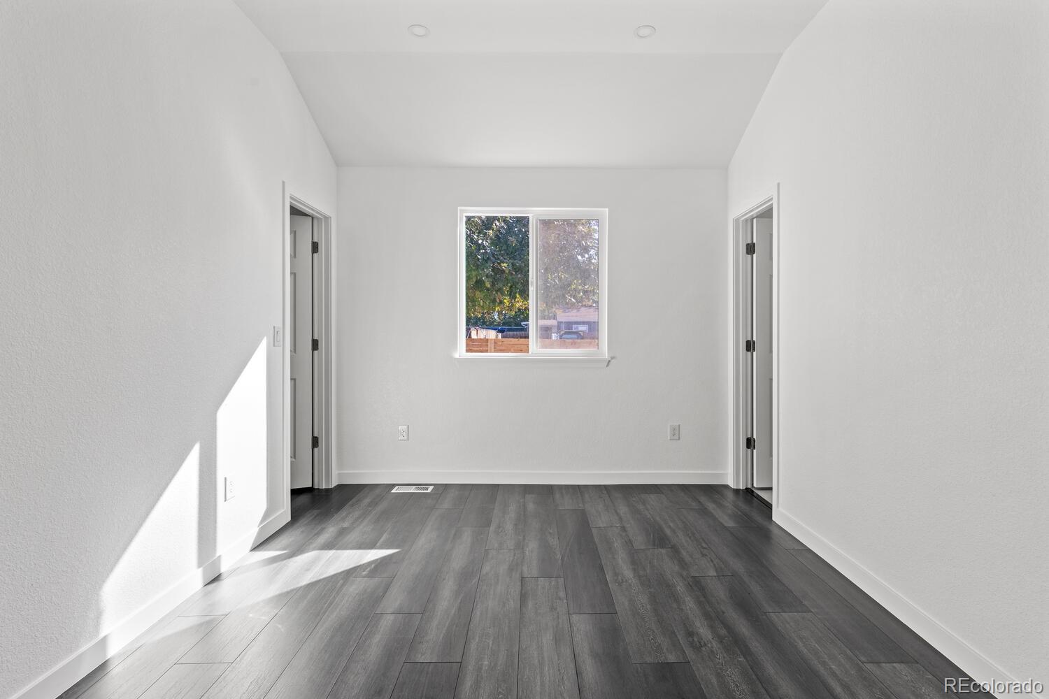 Vacant room with gray plank flooring, a centered window, and two open doorways.