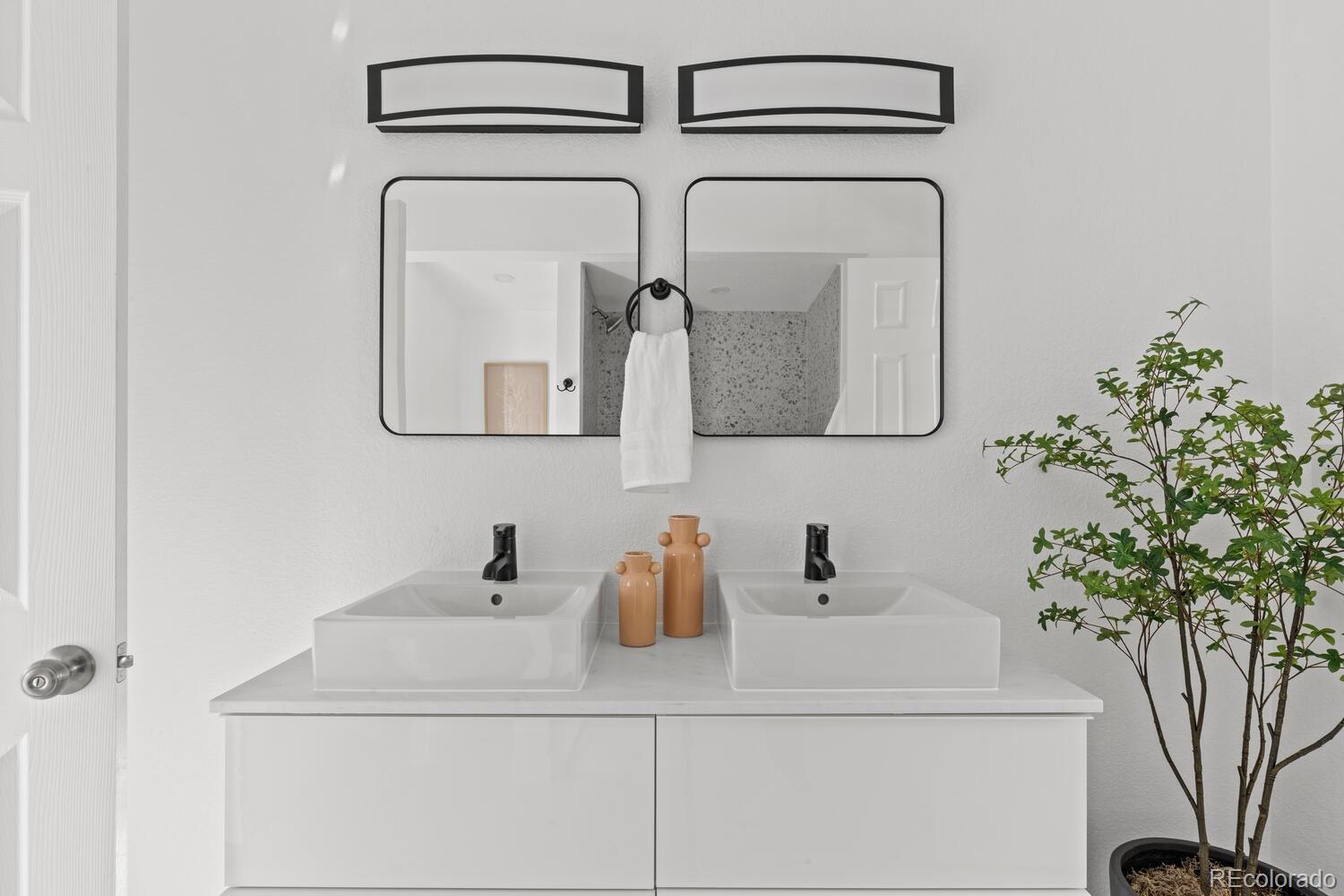 Bathroom with a white double vanity, rectangular mirrors, black fixtures, and a potted plant.