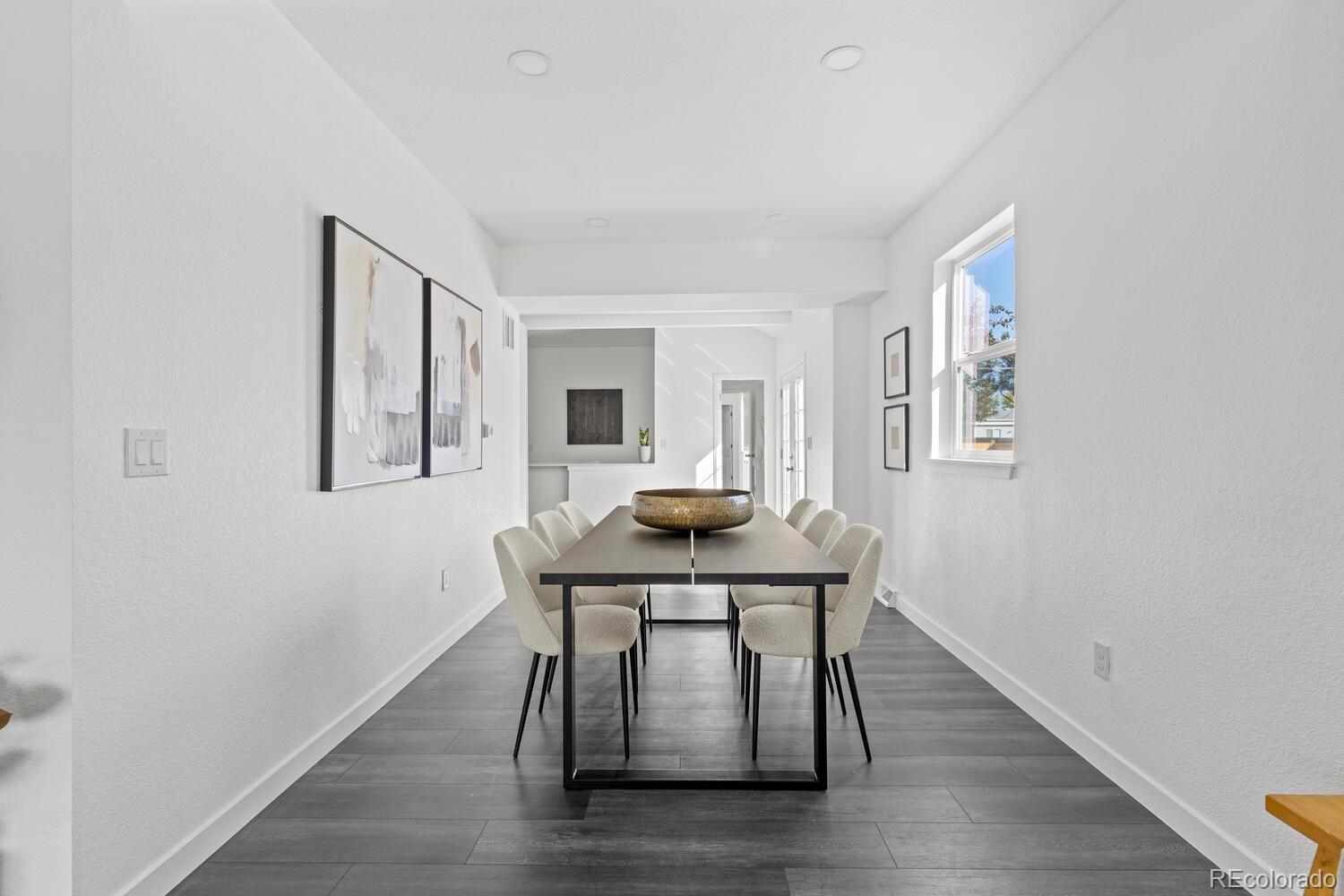 Dining room with a long dark table, cream chairs, gray plank flooring, and a large window.