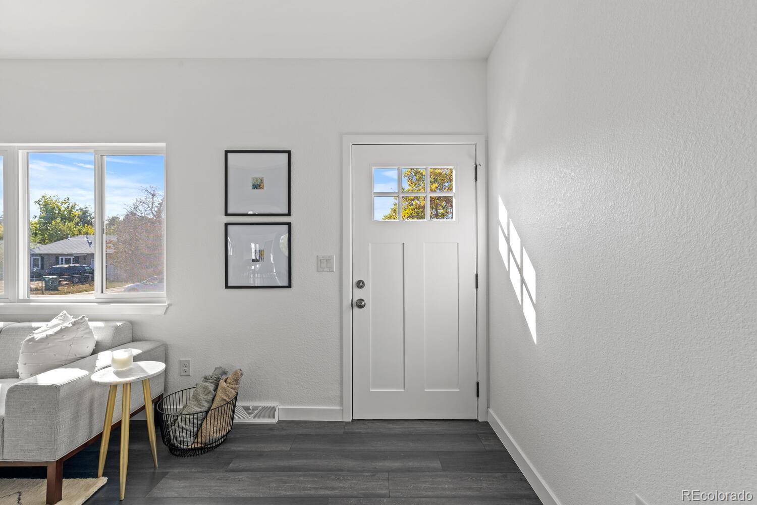 Furnished entryway with a white divided-light door, gray floors, and sunlight streaming through a large window.