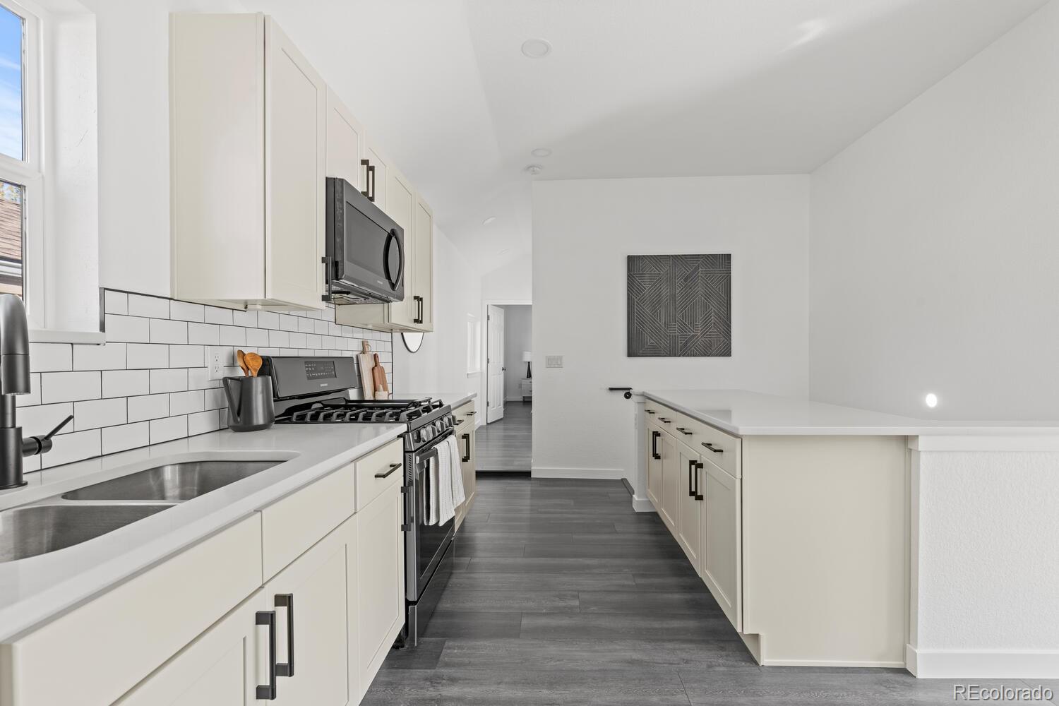 Modern white kitchen with subway tile backsplash, gas range, and long island over dark gray flooring.