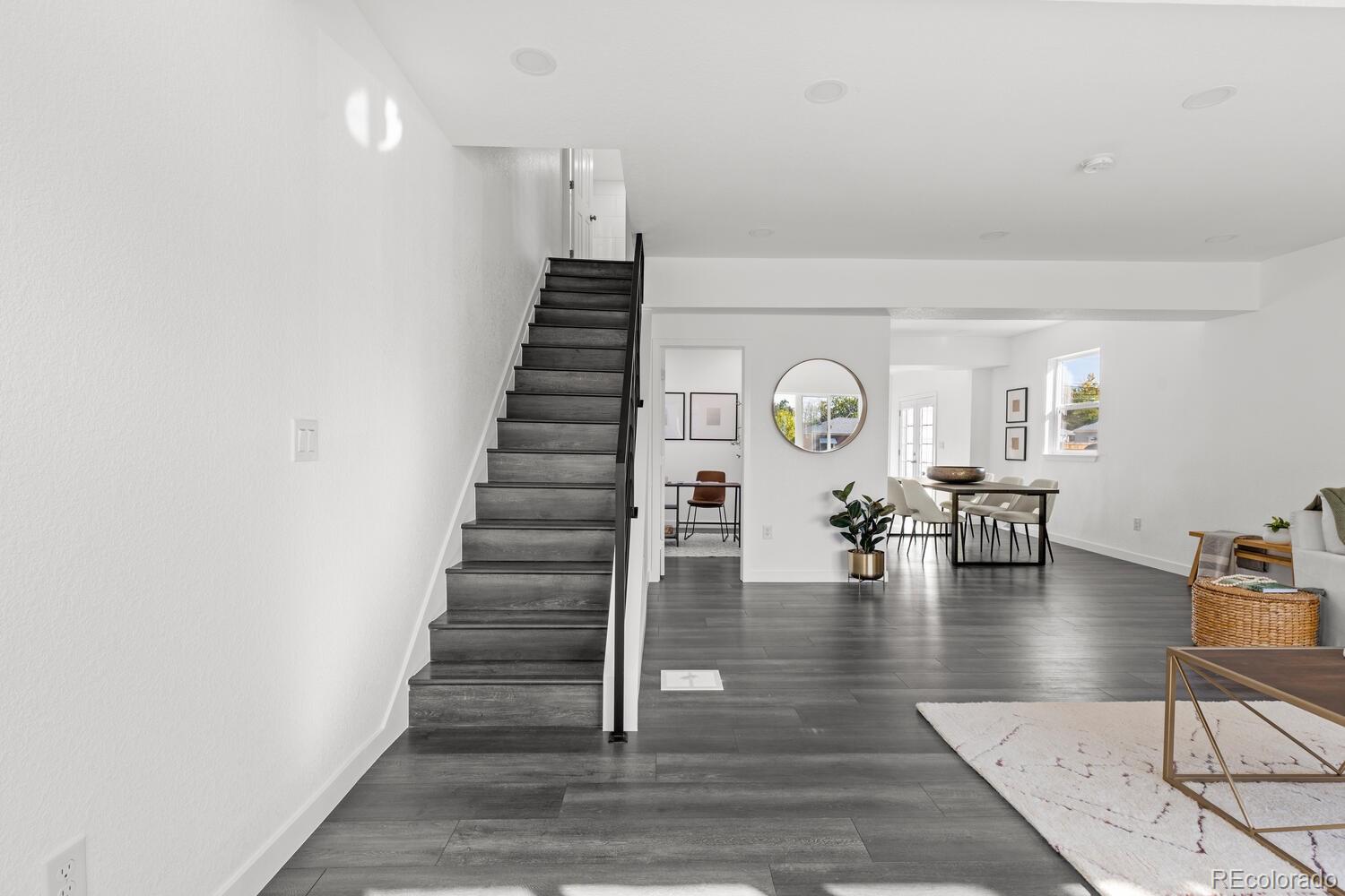 Open living and dining area with dark flooring and a staircase.