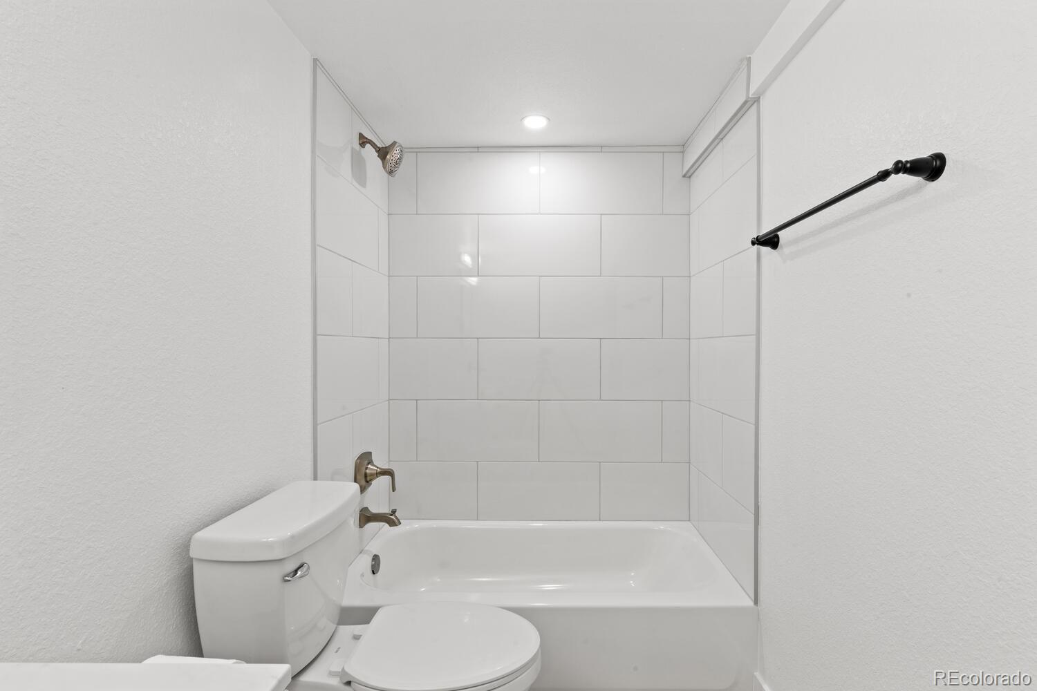 Bathroom with a white tub, large white tile walls, glass shower screen, and black towel bar.