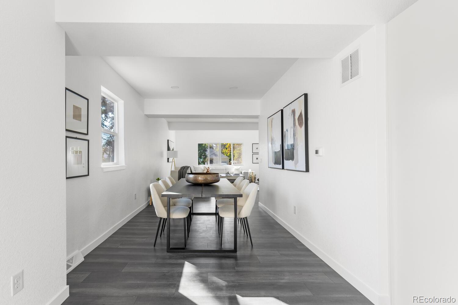 Staged dining room with a dark table, white chairs, and an adjoining living area.