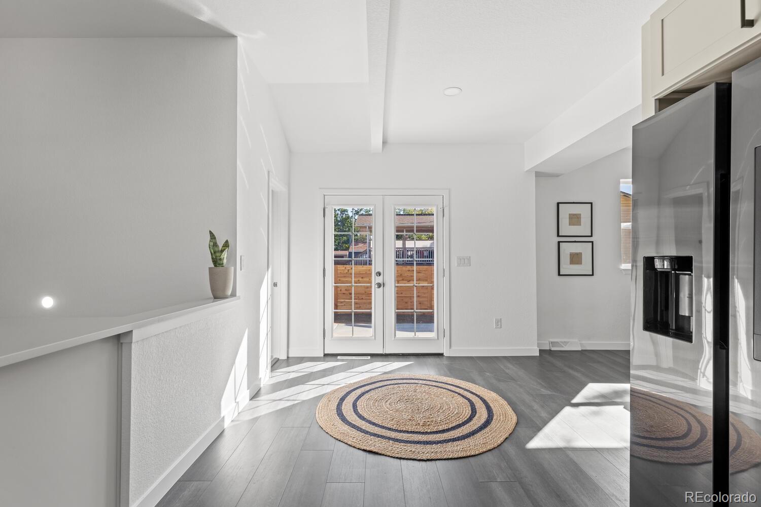 Bright entry with glass-paneled double doors, gray flooring, a round woven rug, and a stainless-steel refrigerator.