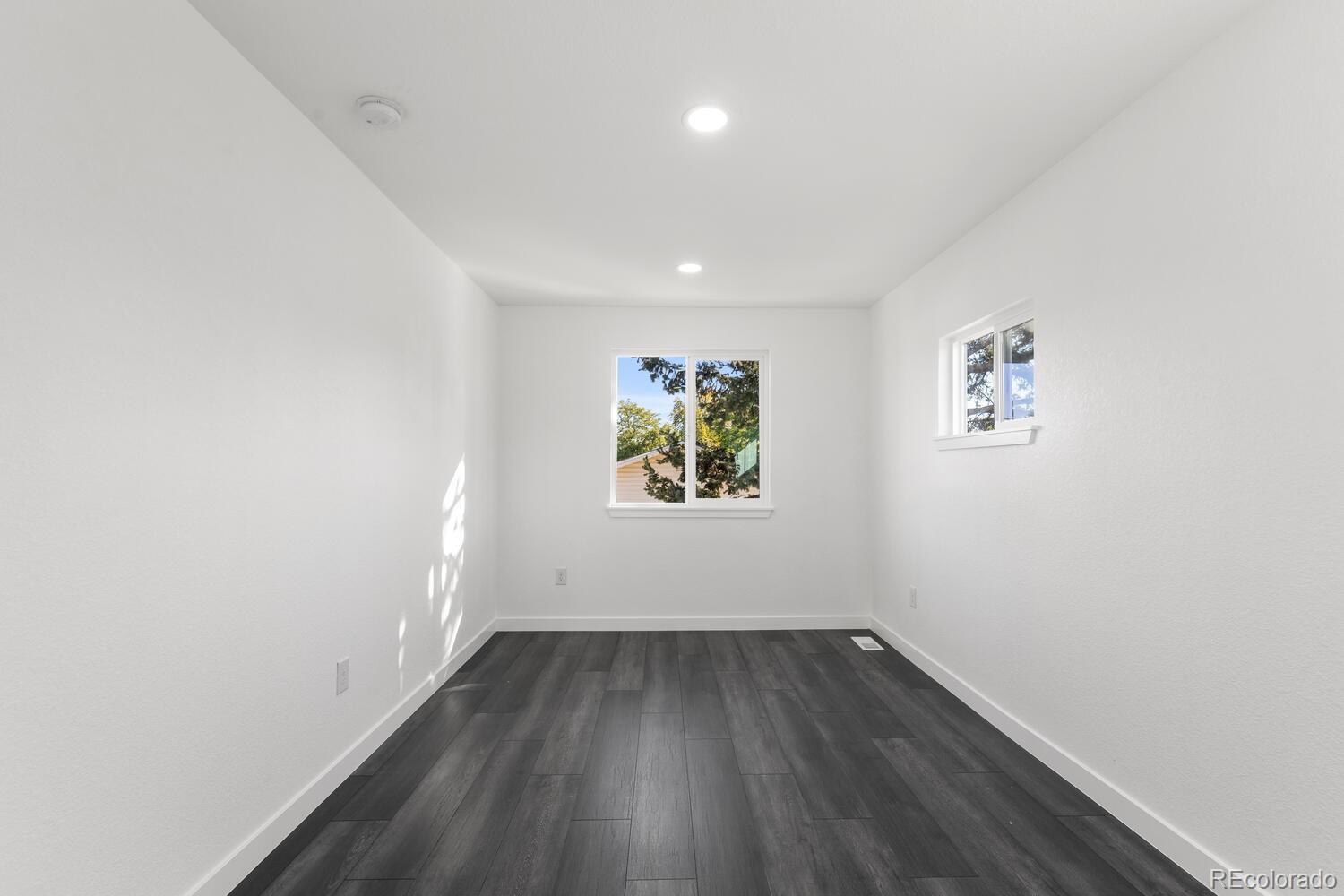 Empty room with dark flooring, white walls, and two windows.
