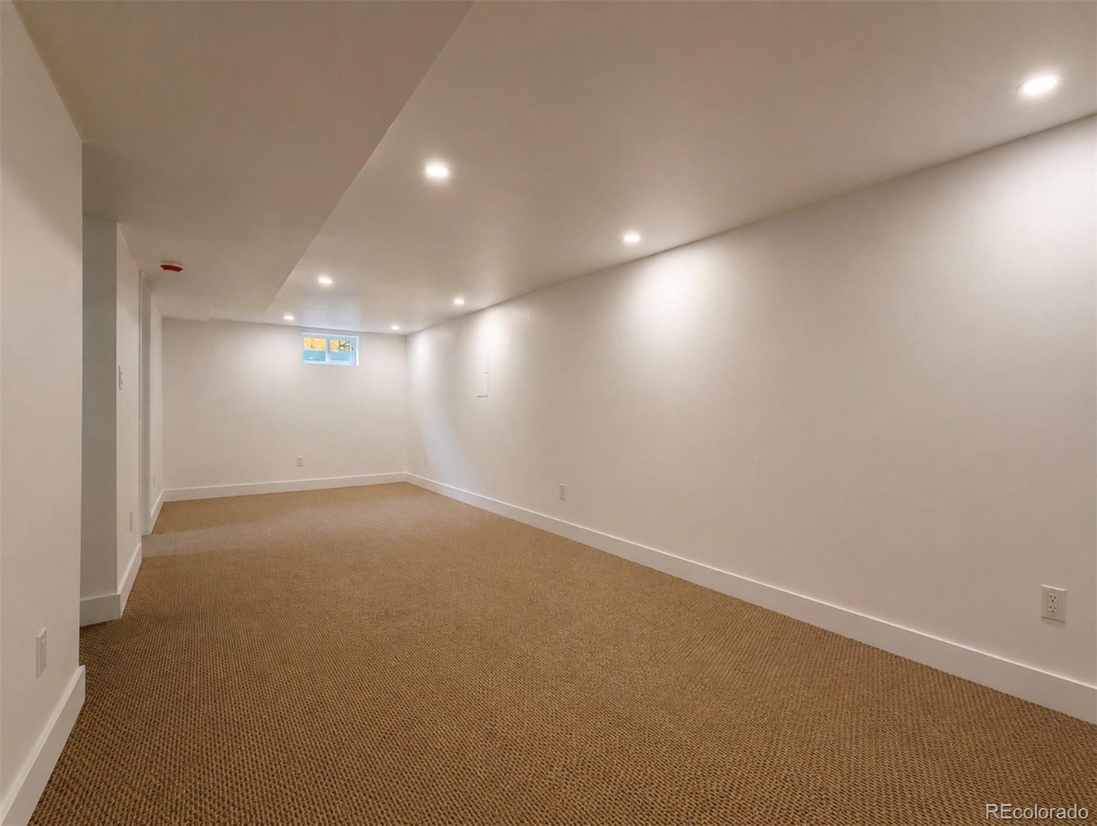 Vacant basement room with tan carpet, recessed lights, and a small high-set window.