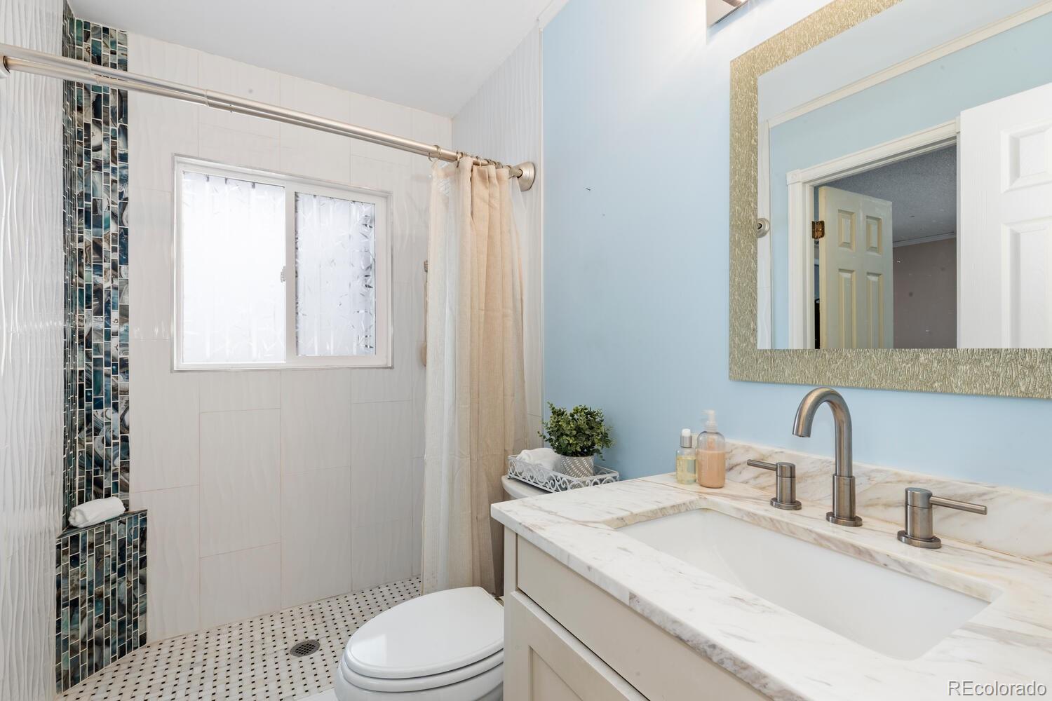 Bathroom with a marble-look vanity and a walk-in shower featuring blue mosaic tile.