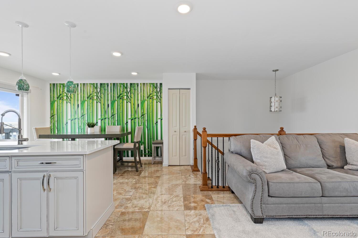 Open-plan kitchen and living room with a gray sectional, white island, and green bamboo mural.