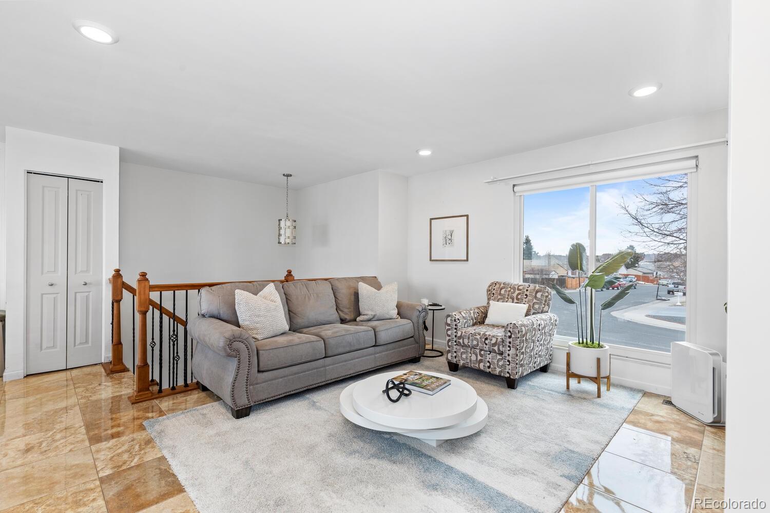 Living room with gray sofa, patterned armchair, and large window overlooking the street.