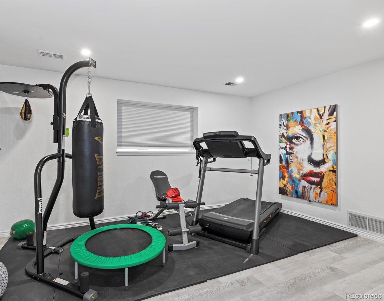 Home gym with treadmill, hanging punching bag, weight bench, and green rebounder.