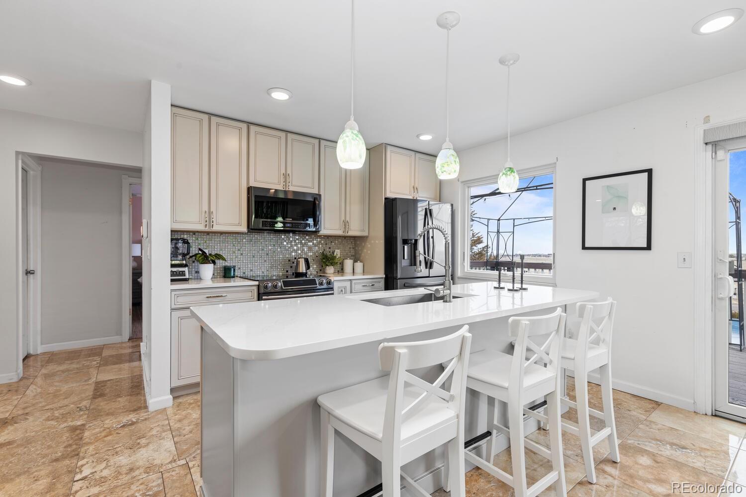Bright kitchen with a large white island, seating for three, cream cabinetry, and stainless steel appliances.