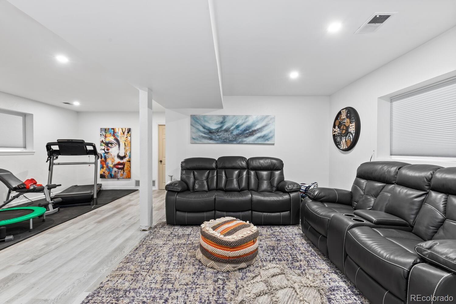 Basement recreation room with black leather seating, a patterned rug, and treadmill.