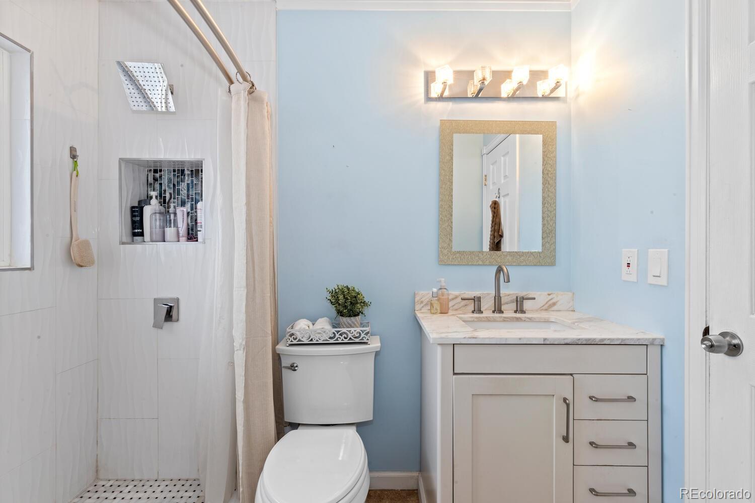 Bathroom with a tiled walk-in shower and a light vanity against a pale blue wall.