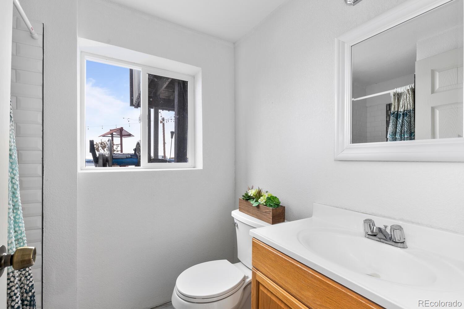 Bathroom with a wood-front vanity, white fixtures, tiled shower, and daylight from a window.