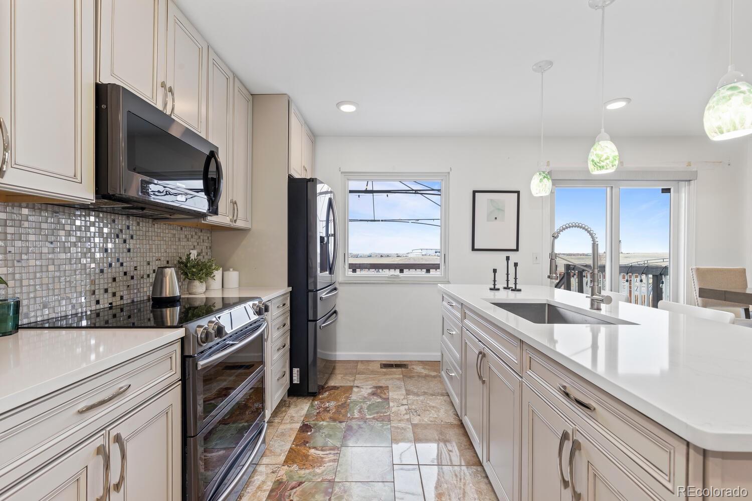 Bright kitchen with a large white island, stainless steel appliances, and windows overlooking the outdoors.