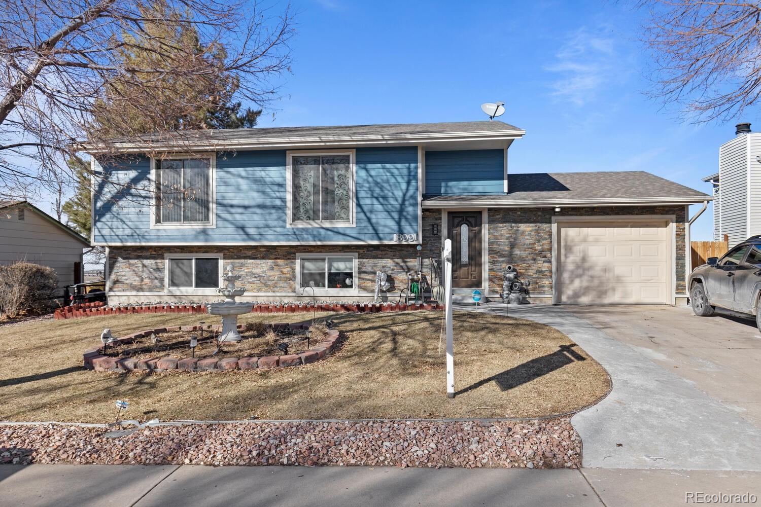 Blue split-level home with stone veneer, an attached garage, and a curved driveway.