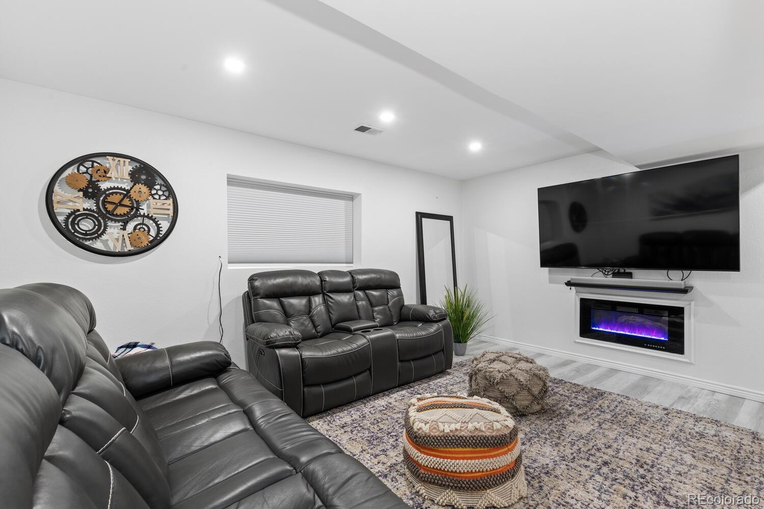 Living room with black leather reclining sofas, a wall-mounted television, and an electric fireplace.