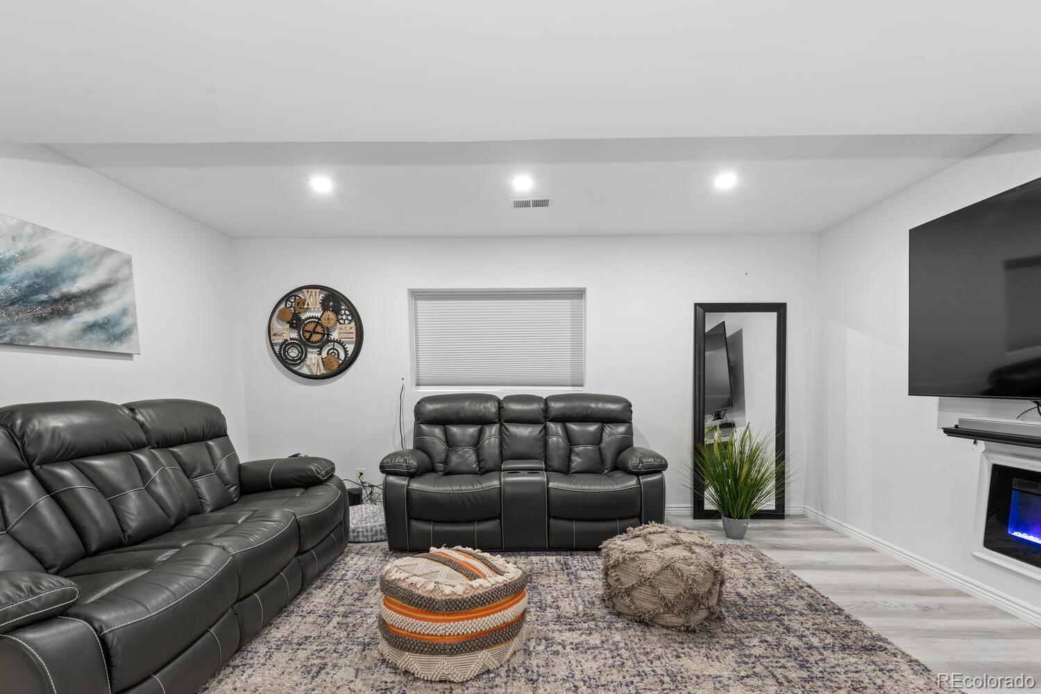 Living room with black leather reclining sofas, a wall-mounted TV, and an electric fireplace.