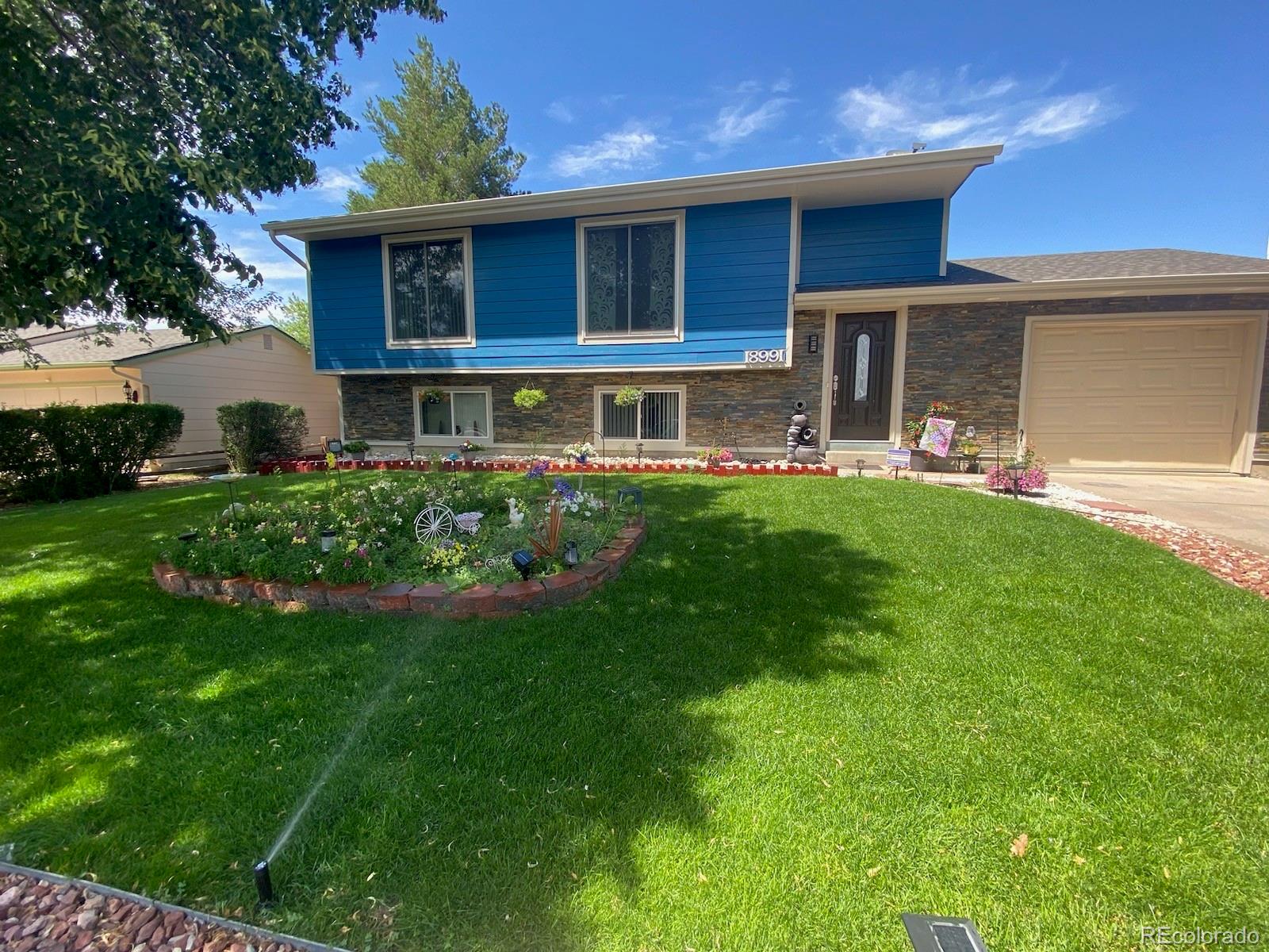 Blue split-level home with stone veneer, an attached garage, and a flower garden in front.