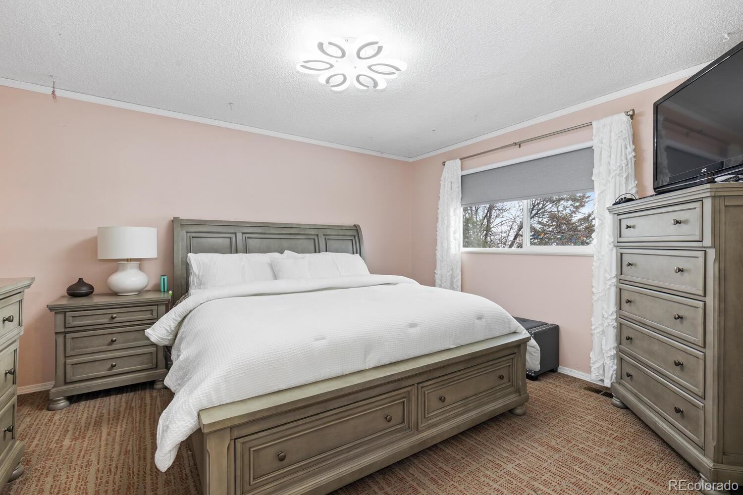 Furnished bedroom with a gray wood bed, matching dressers, and a window with white curtains.