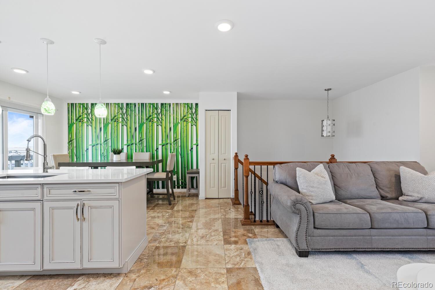 Open-plan kitchen and living area with a white island, gray sofa, and bamboo mural.