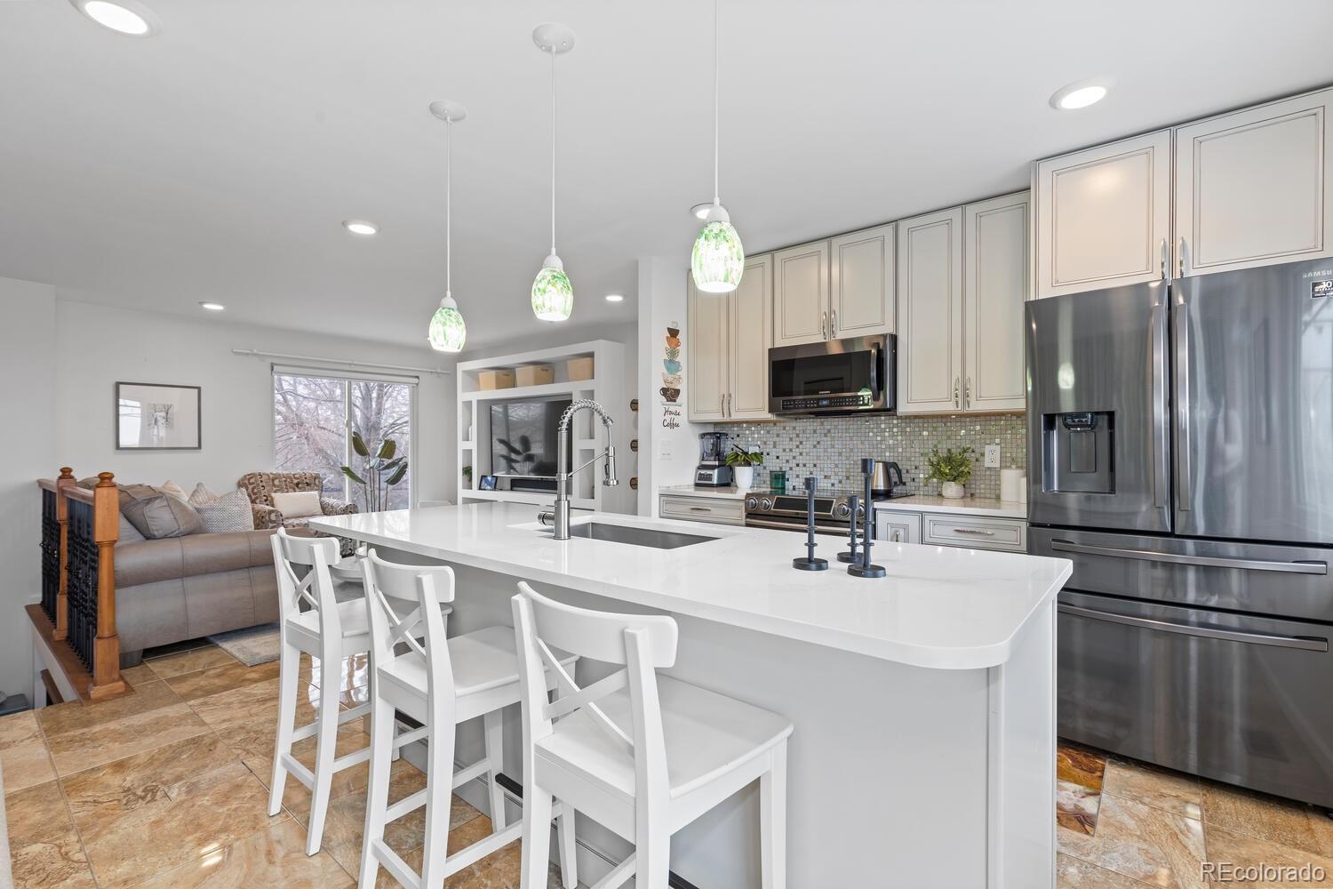 Bright kitchen with a large white island, pendant lights, and stainless steel appliances.