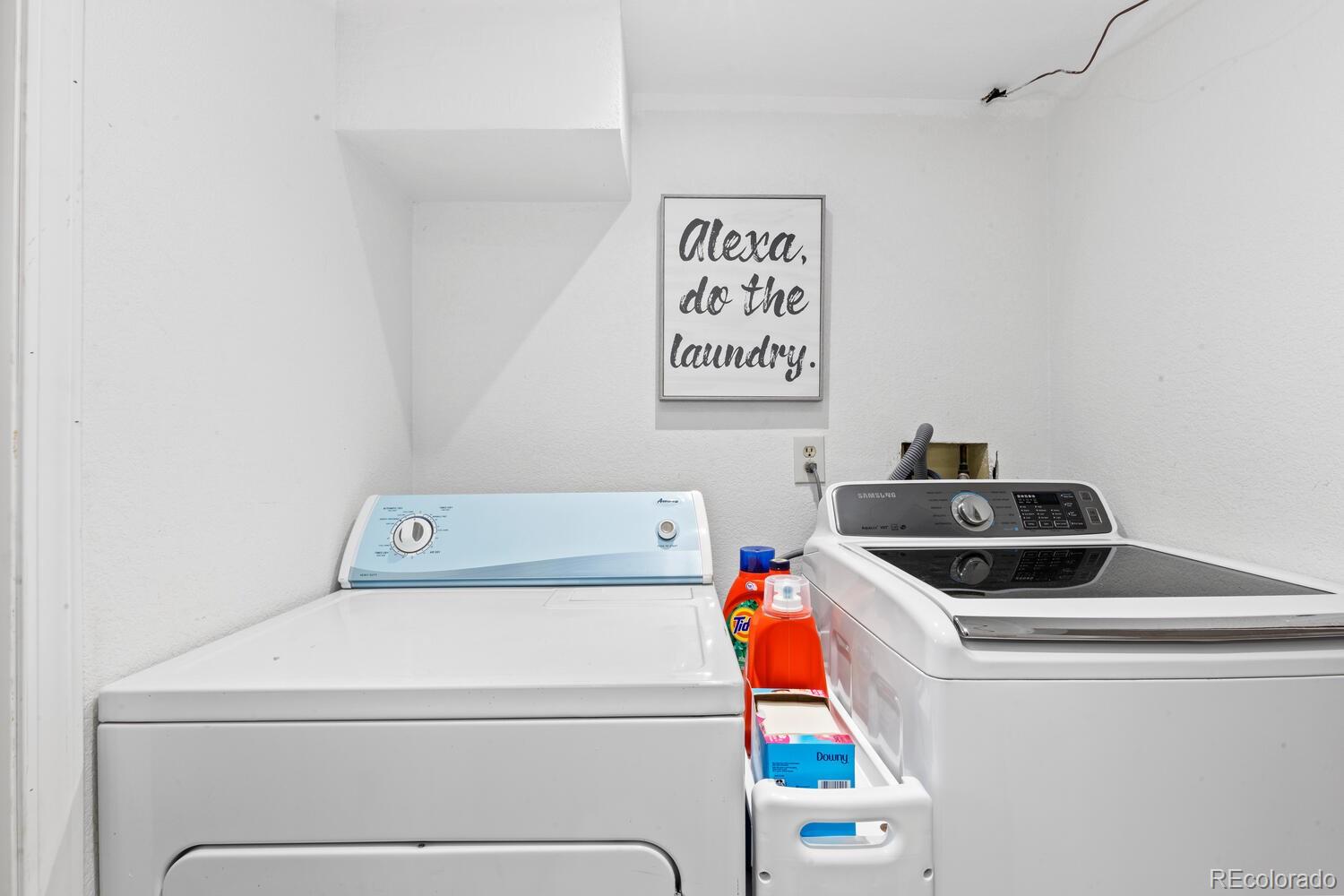 Laundry room with a white washer and Samsung dryer beneath a framed “Alexa, do the laundry” sign.
