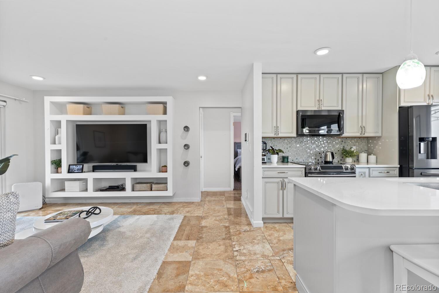 Open-plan living room and kitchen with a built-in TV wall, white cabinetry, and a large island.