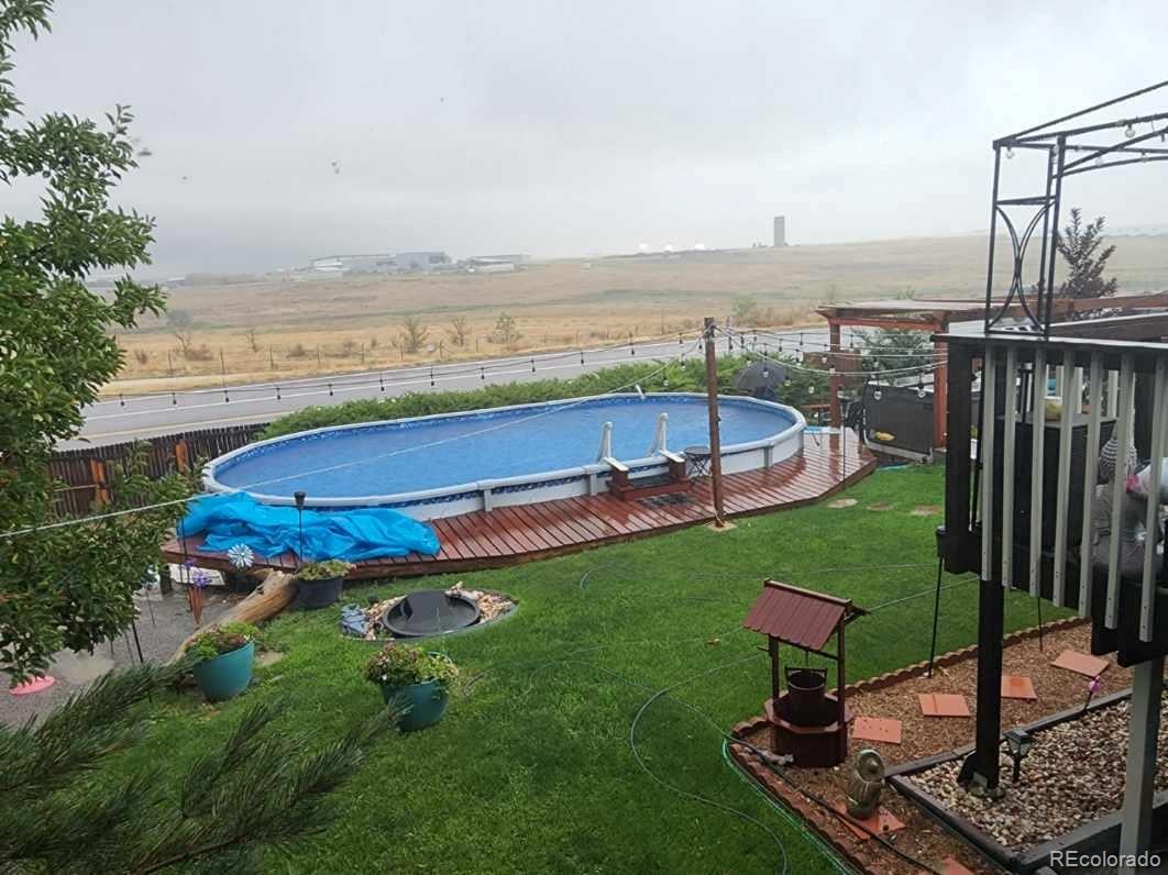 Backyard pool on a raised wooden deck beside a green lawn and fire pit.