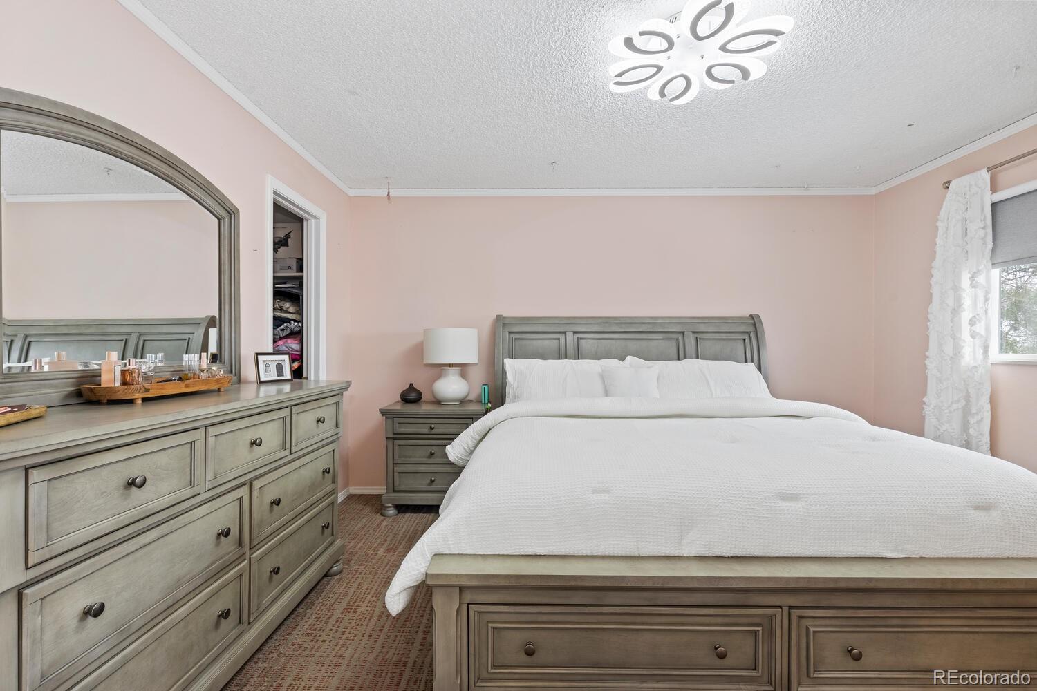 Bedroom with a large white bed, gray wood furniture, an arched mirror, and pale pink walls.