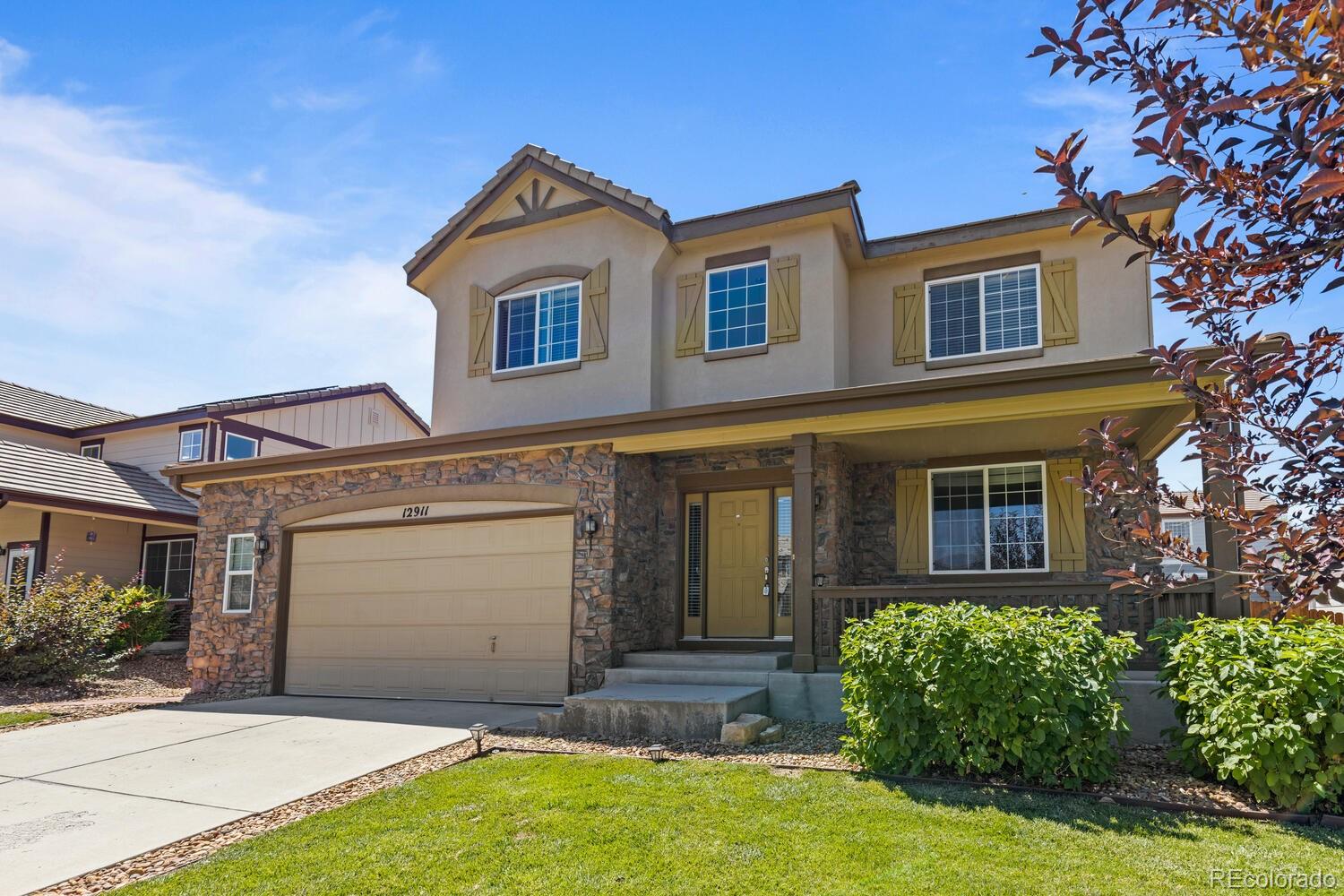 Two-story home with stone facade, tan garage door, covered porch, and landscaped front lawn.