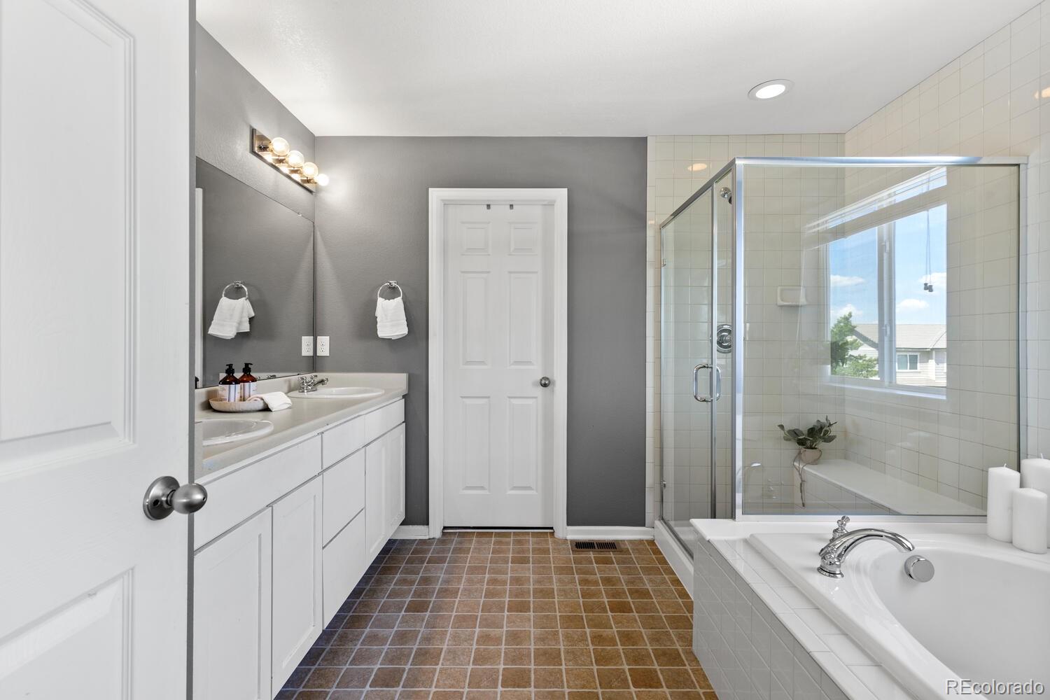 Bathroom with a double-sink vanity, glass shower, and built-in tub beside a window.