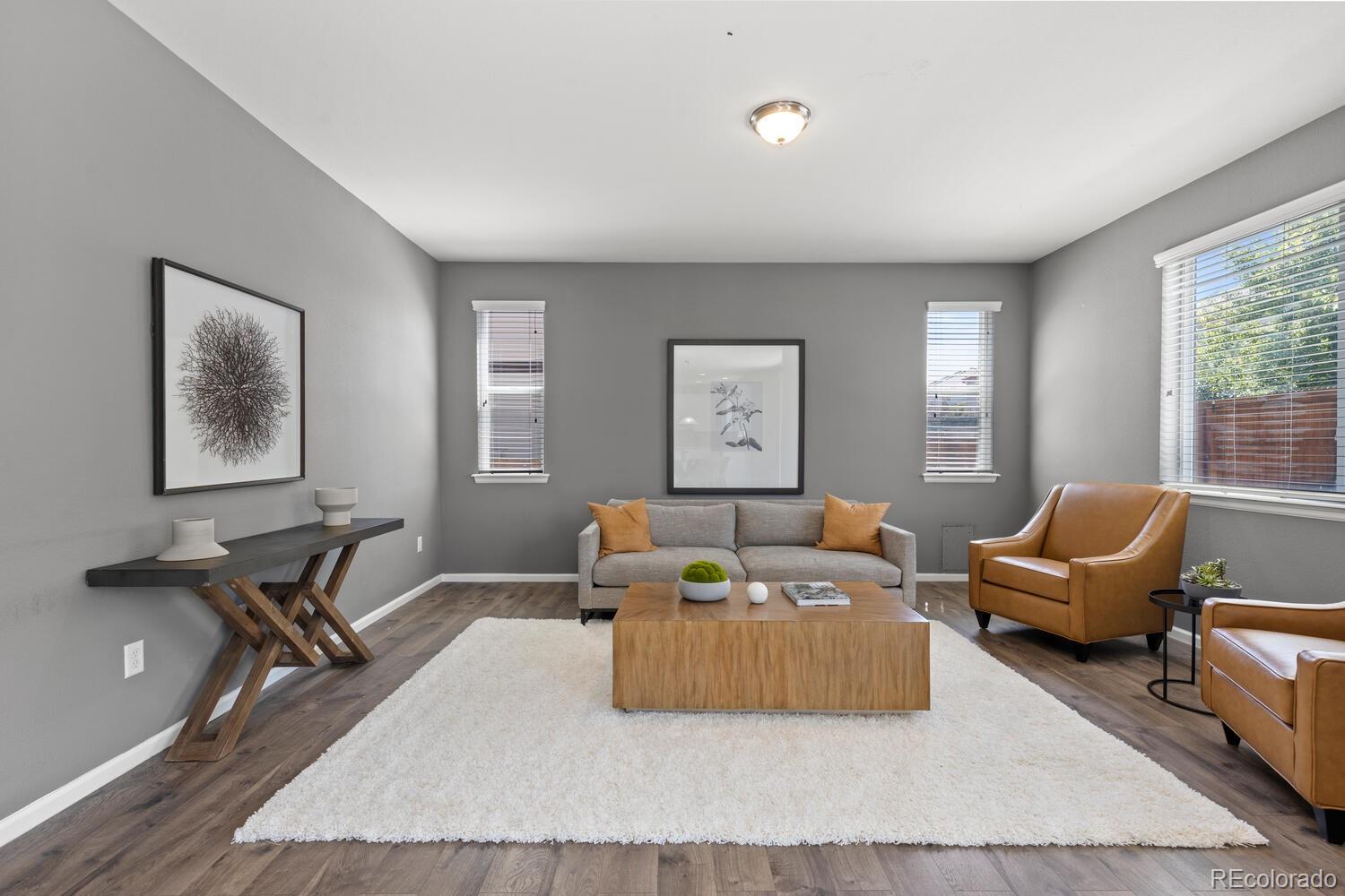 Staged living room with gray sofa, caramel leather chairs, and a large white rug.