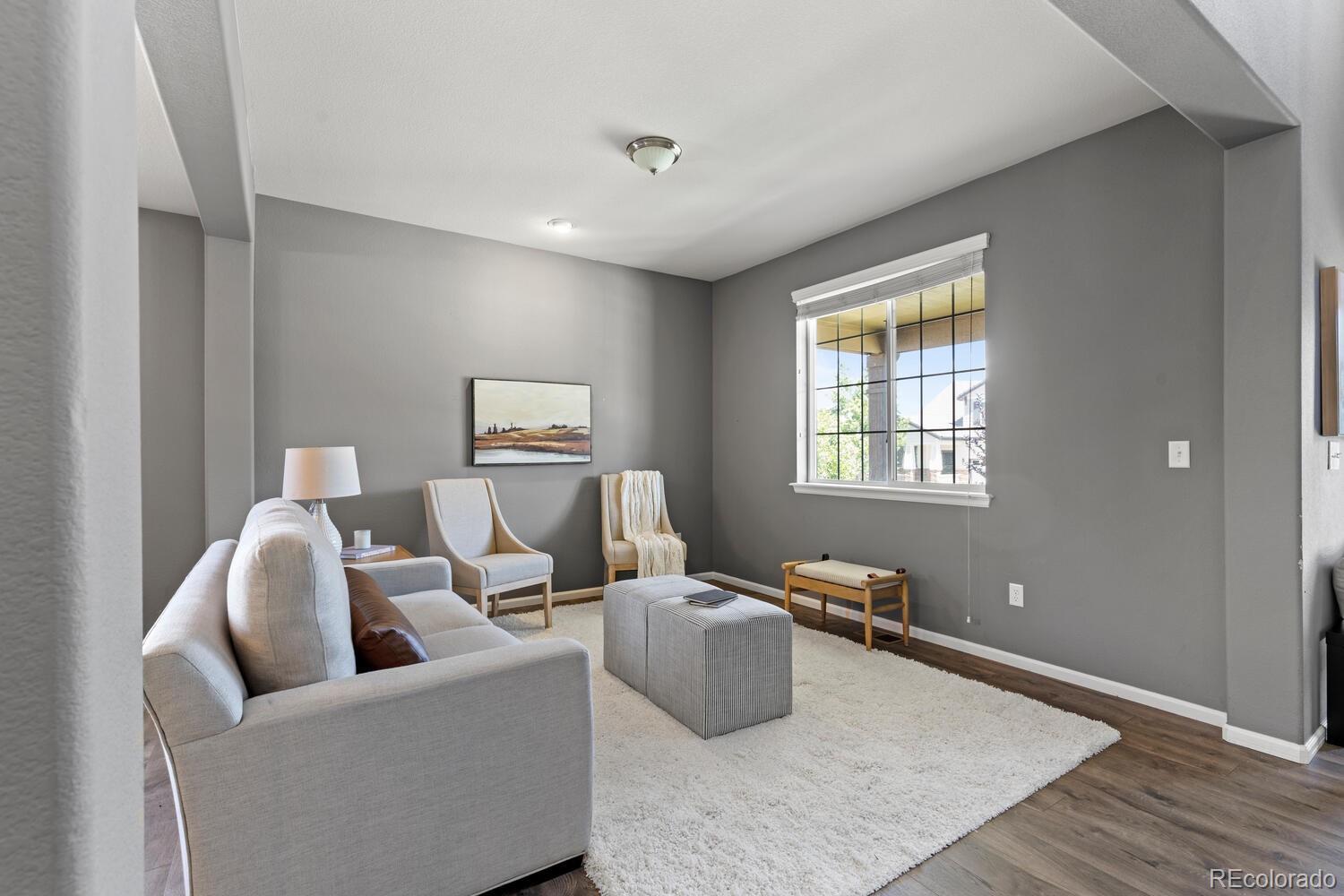 Staged living room with a light sofa, white rug, gray walls, and a large gridded window.