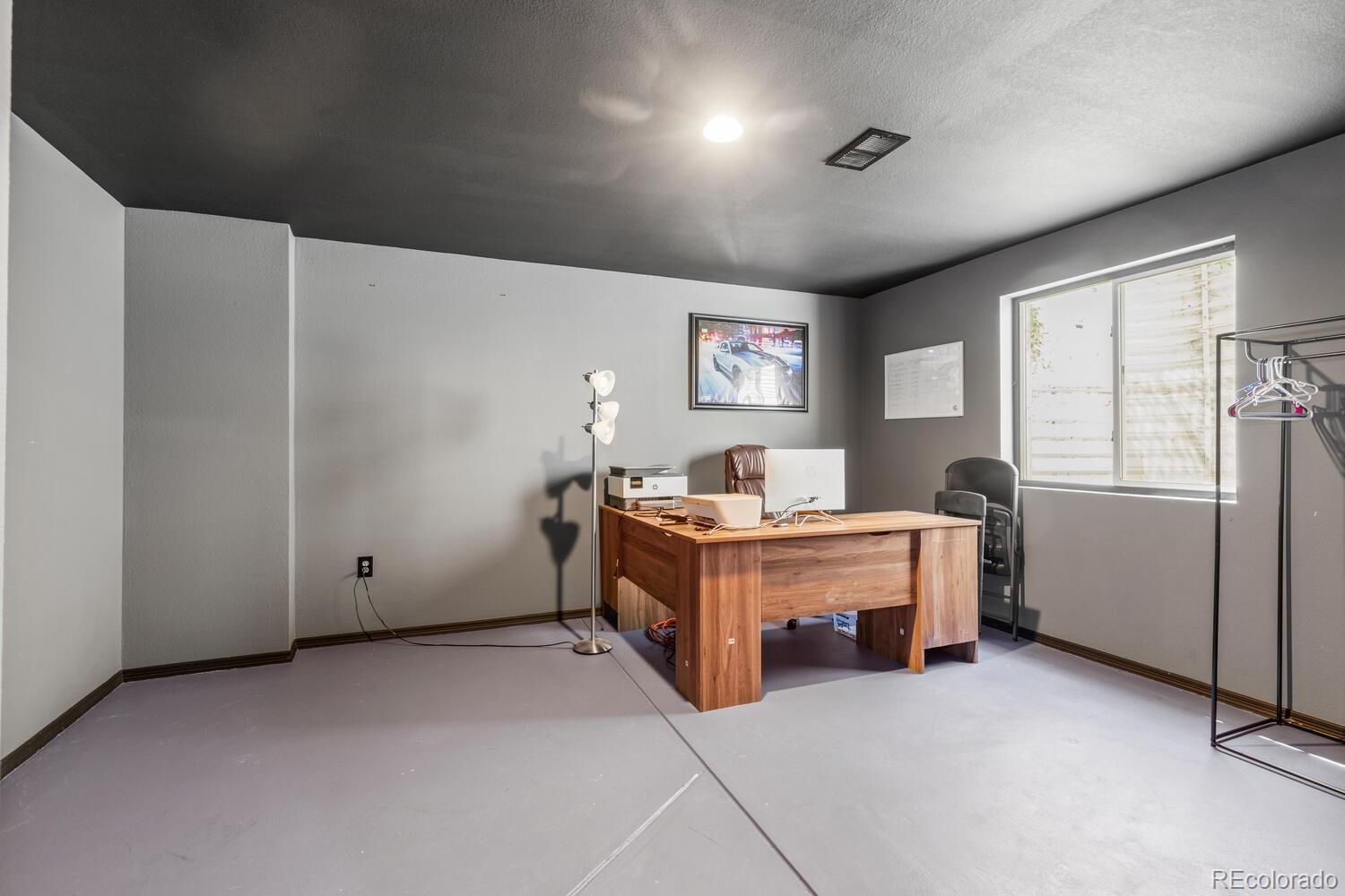 Office with a wooden desk and computer, clothing rack, and large window.