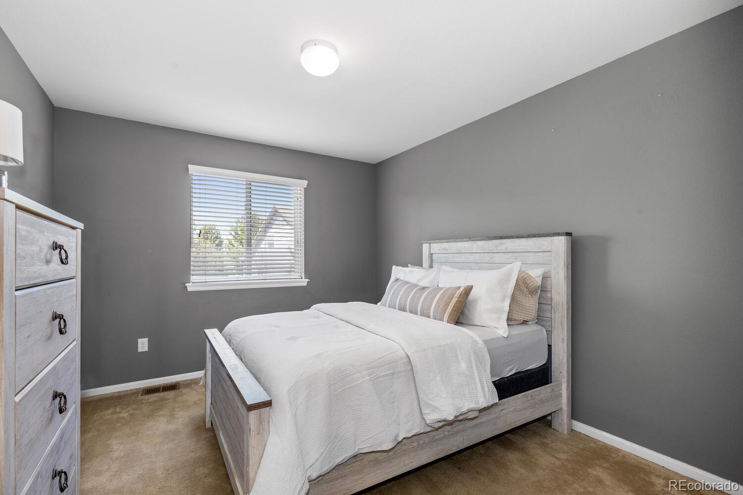 Bedroom with a light wood bed, white bedding, gray walls, and a window with blinds.
