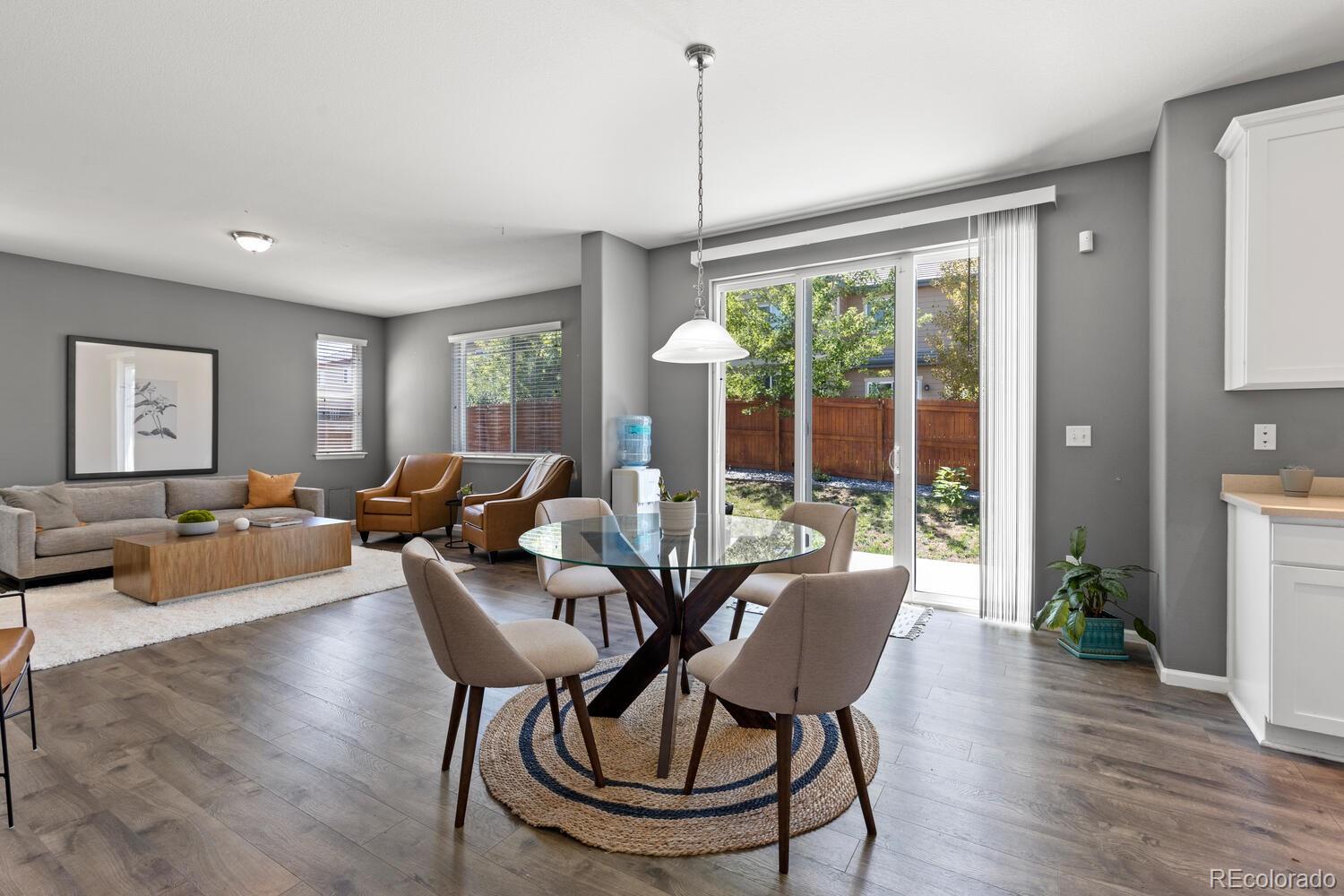 Open-plan living and dining room with a glass table and sliding doors to a fenced backyard.