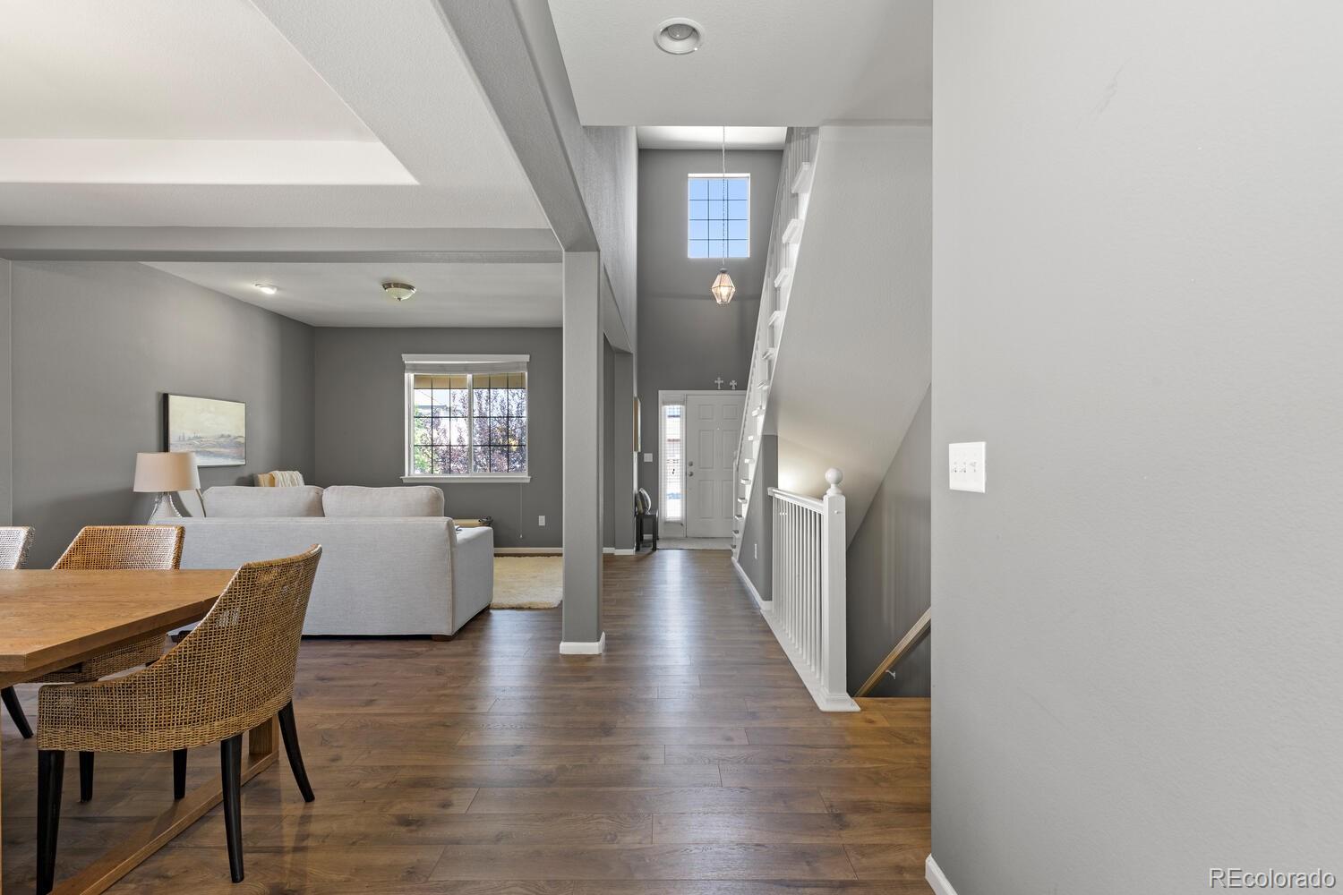 Living and dining area with wood floors, woven dining chairs, and a staircase beside the entry hall.