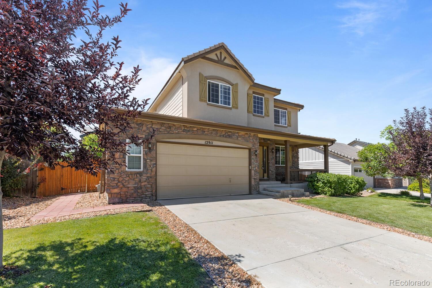 Two-story house with stone facade, two-car garage, covered porch, and landscaped front lawn.