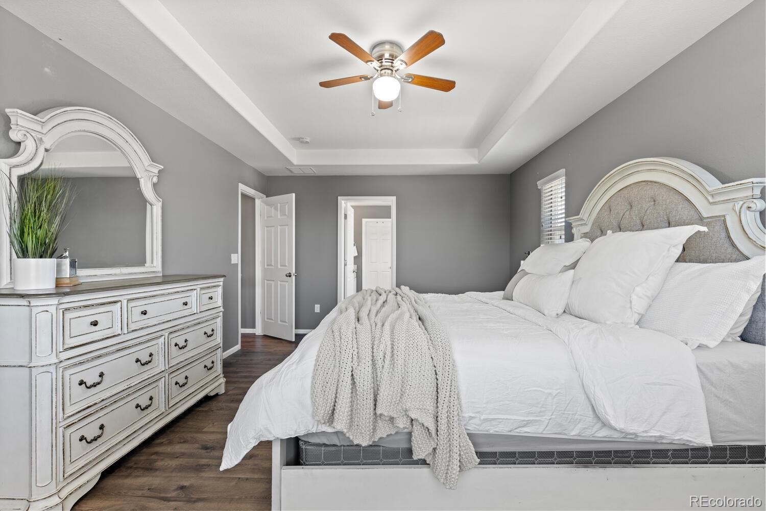 Bedroom with a white bed, ornate headboard, matching dresser and mirror, and tray ceiling.