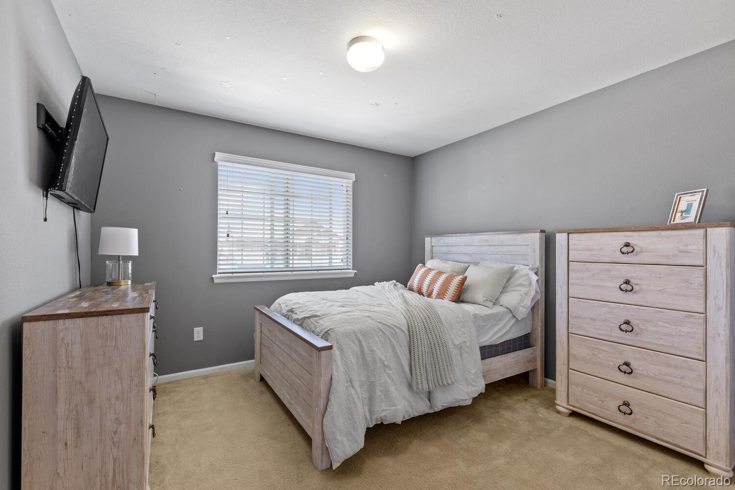 Furnished bedroom with a light wood bed, white bedding, matching dresser, and wall-mounted television.