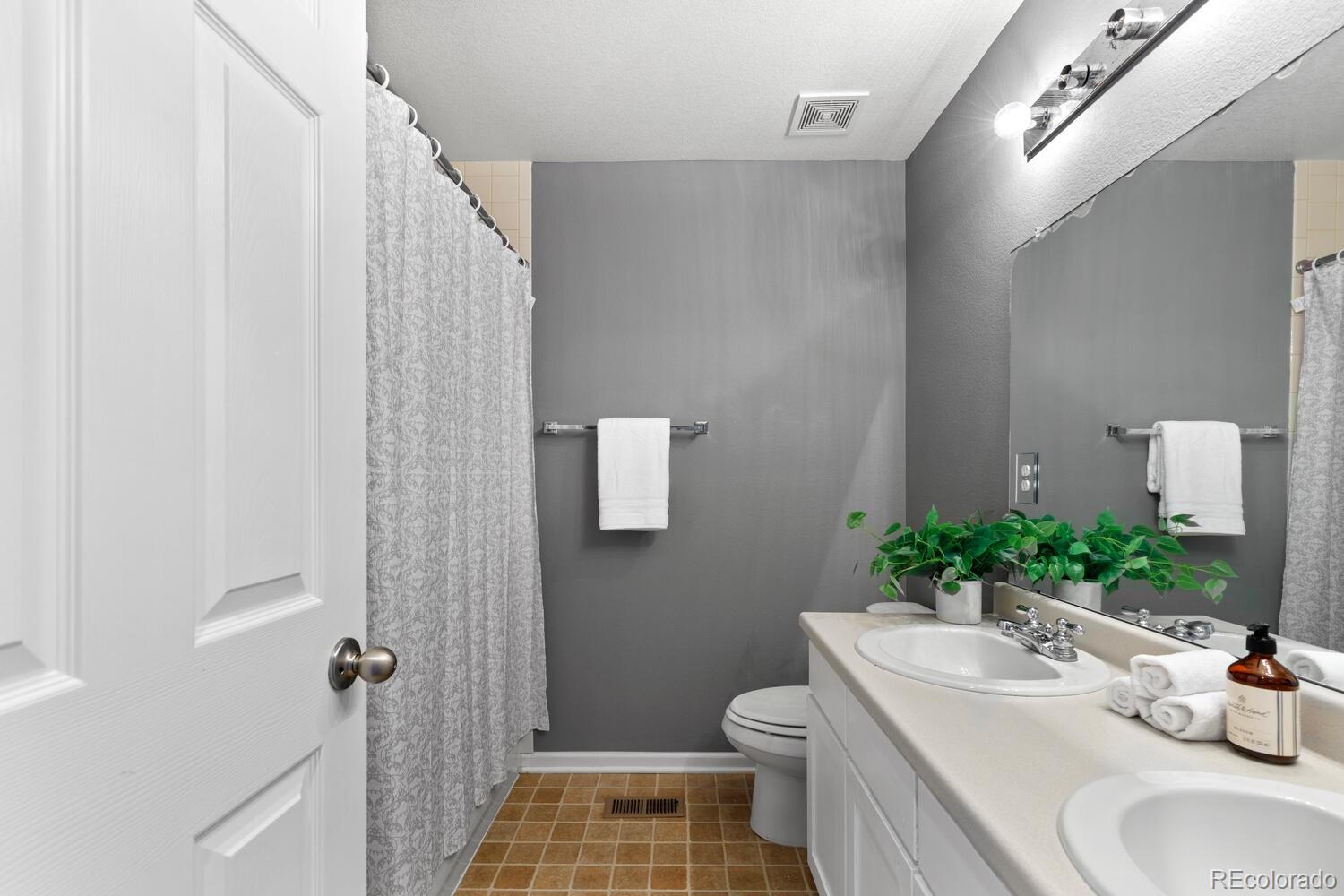 Bathroom with a double-sink vanity, large mirror, and patterned shower curtain.
