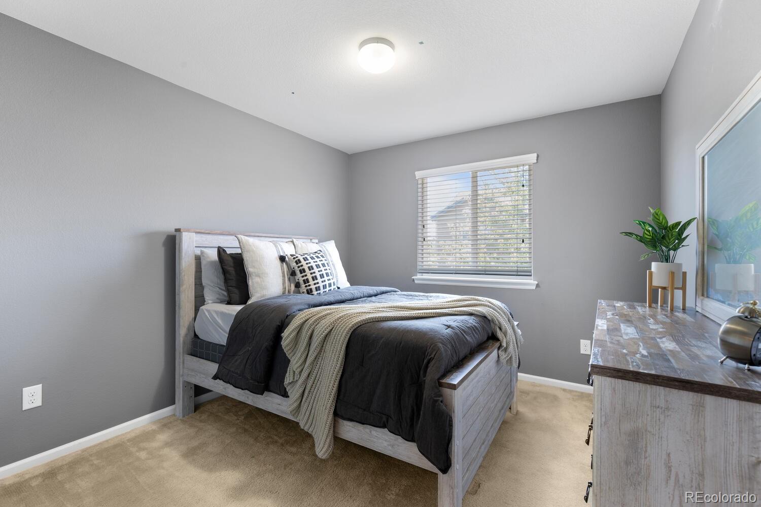 Furnished bedroom with a gray wood bed, dark bedding, window blinds, and matching dresser.