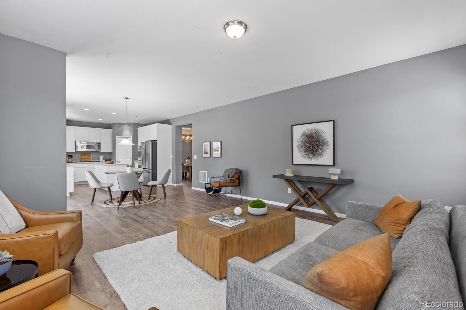 Open-plan living room and kitchen with a gray sofa, leather chairs, and white cabinetry.
